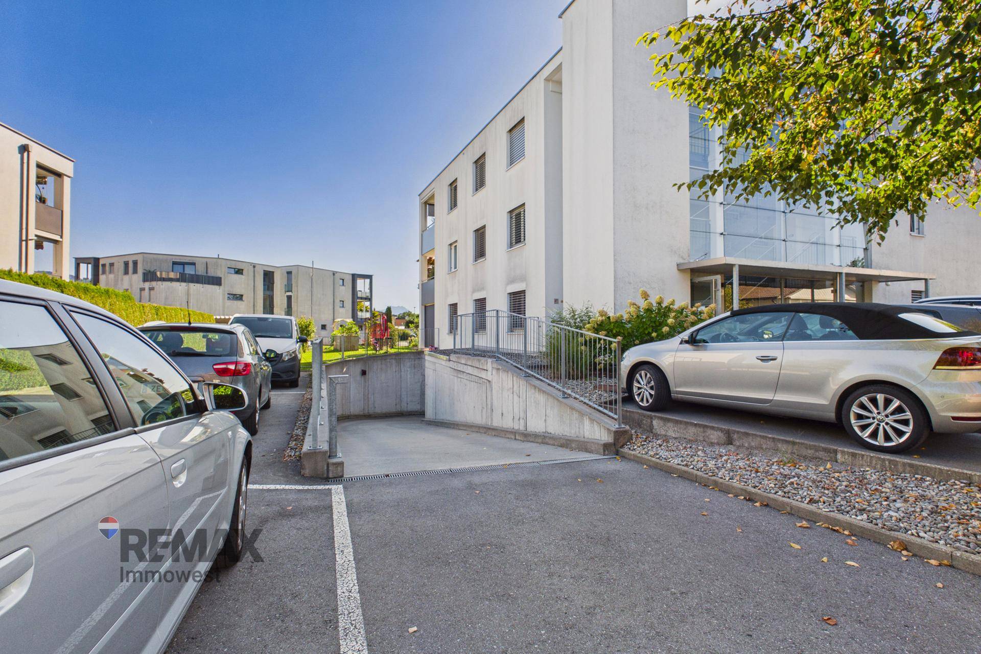 Außenansicht des Gebäudes mit Parkplätzen und Zufahrt zur Tiefgarage.