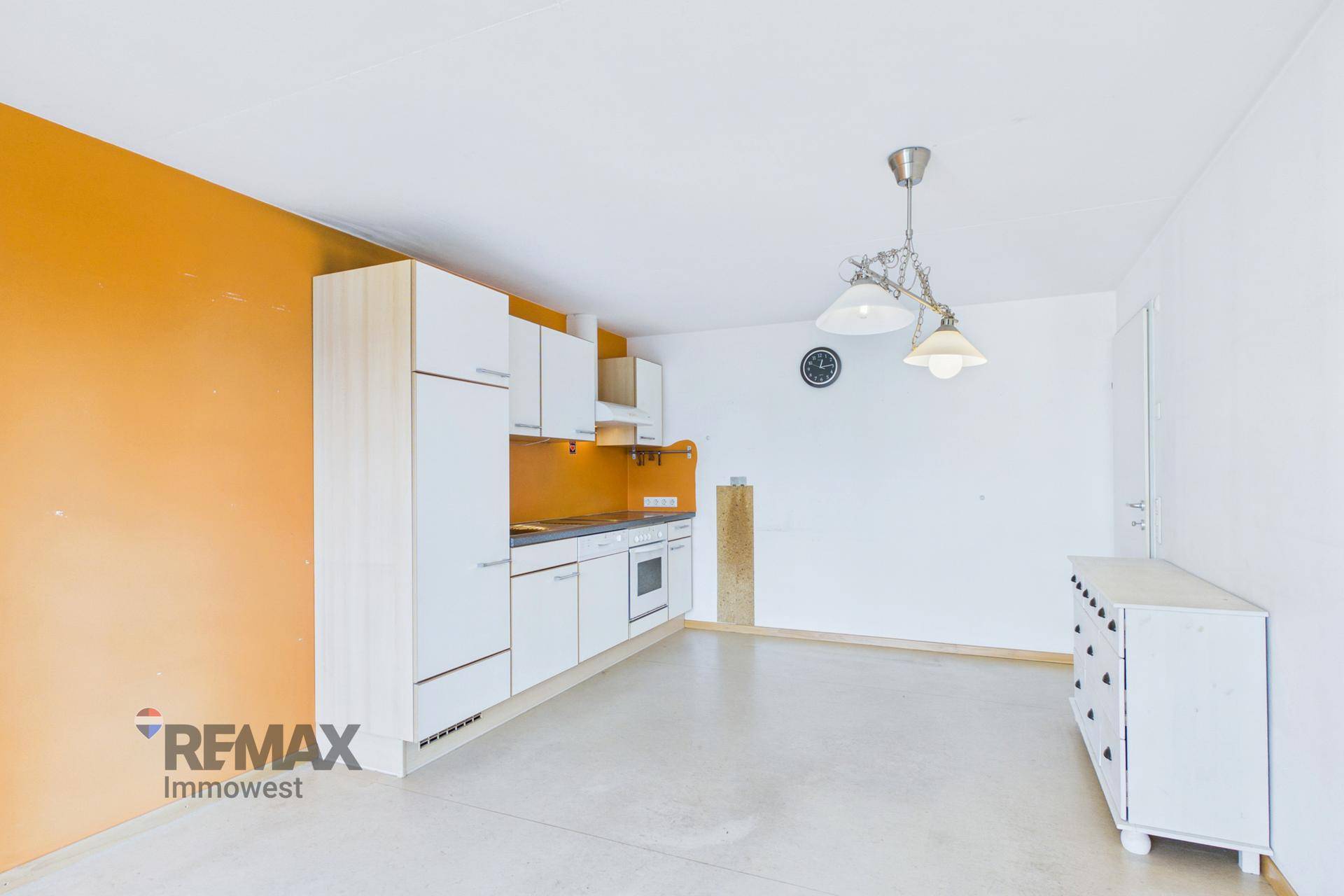 Leere Küche mit weißen Schränken, orangefarbener Wand und Platz für einen Essbereich.
