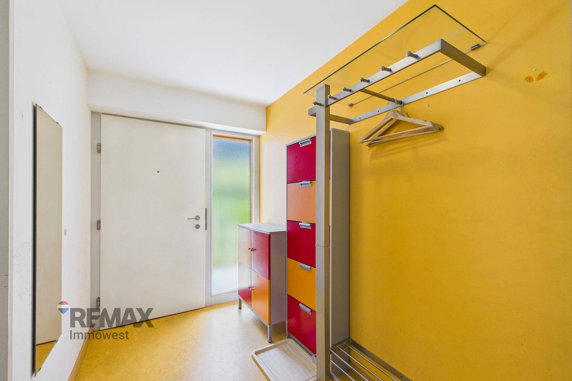 Eingangsbereich mit gelber Wand, Spiegel und Garderobe.