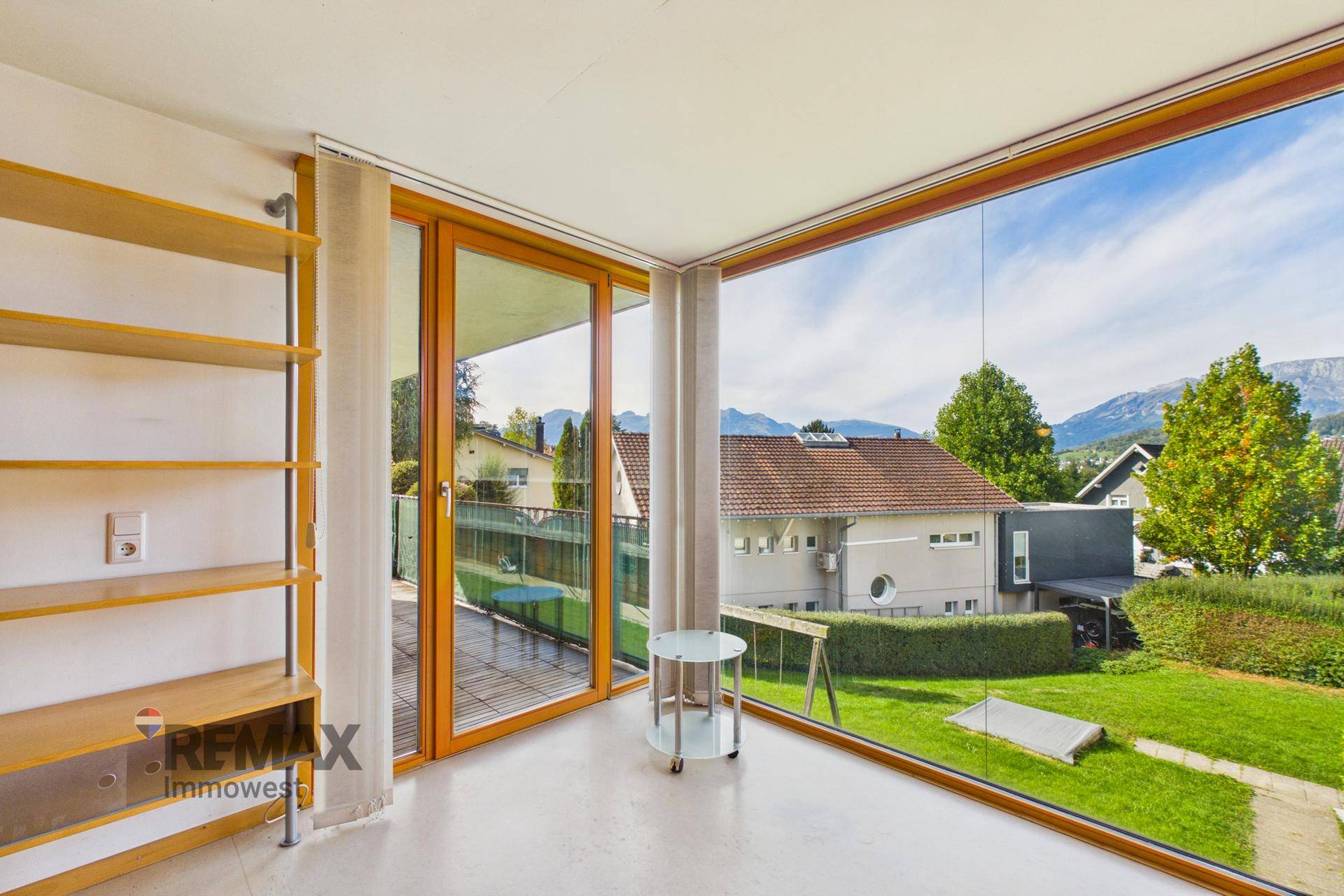 Heller Raum mit großen Fenstern, Holzboden und Zugang zu einem Außenbereich.