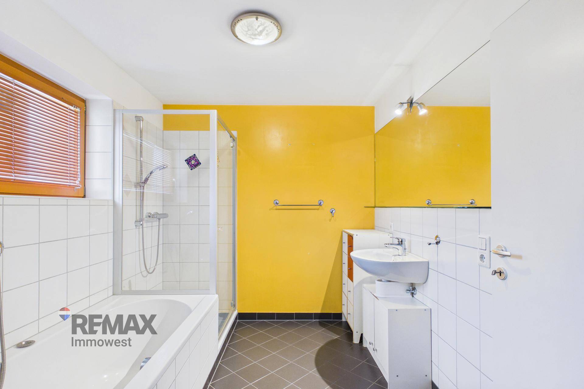 Badezimmer mit Badewanne, Dusche, Waschbecken und gelber Akzentwand.