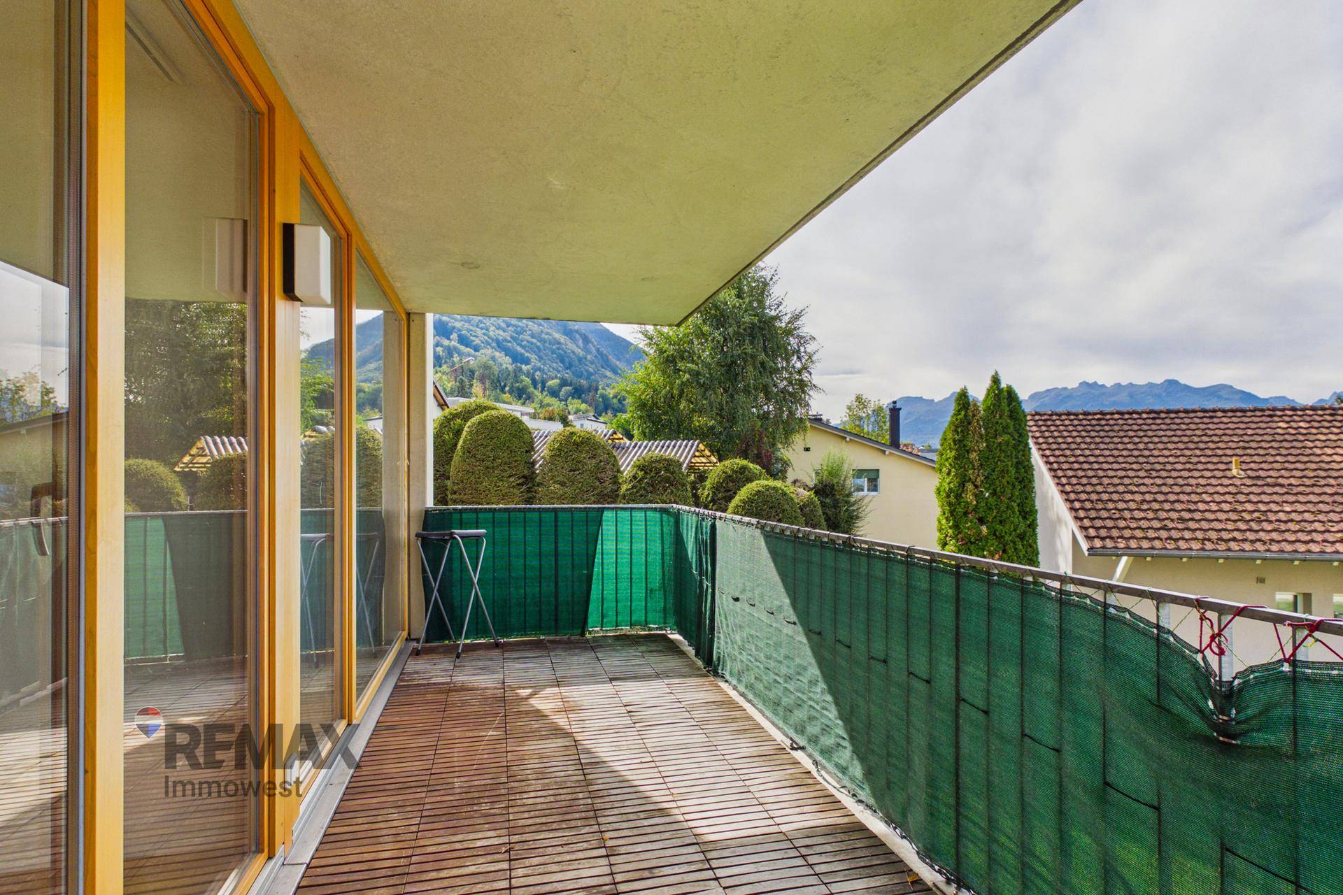Langer Balkon mit Holzboden, grüner Sichtschutz und Bergblick.