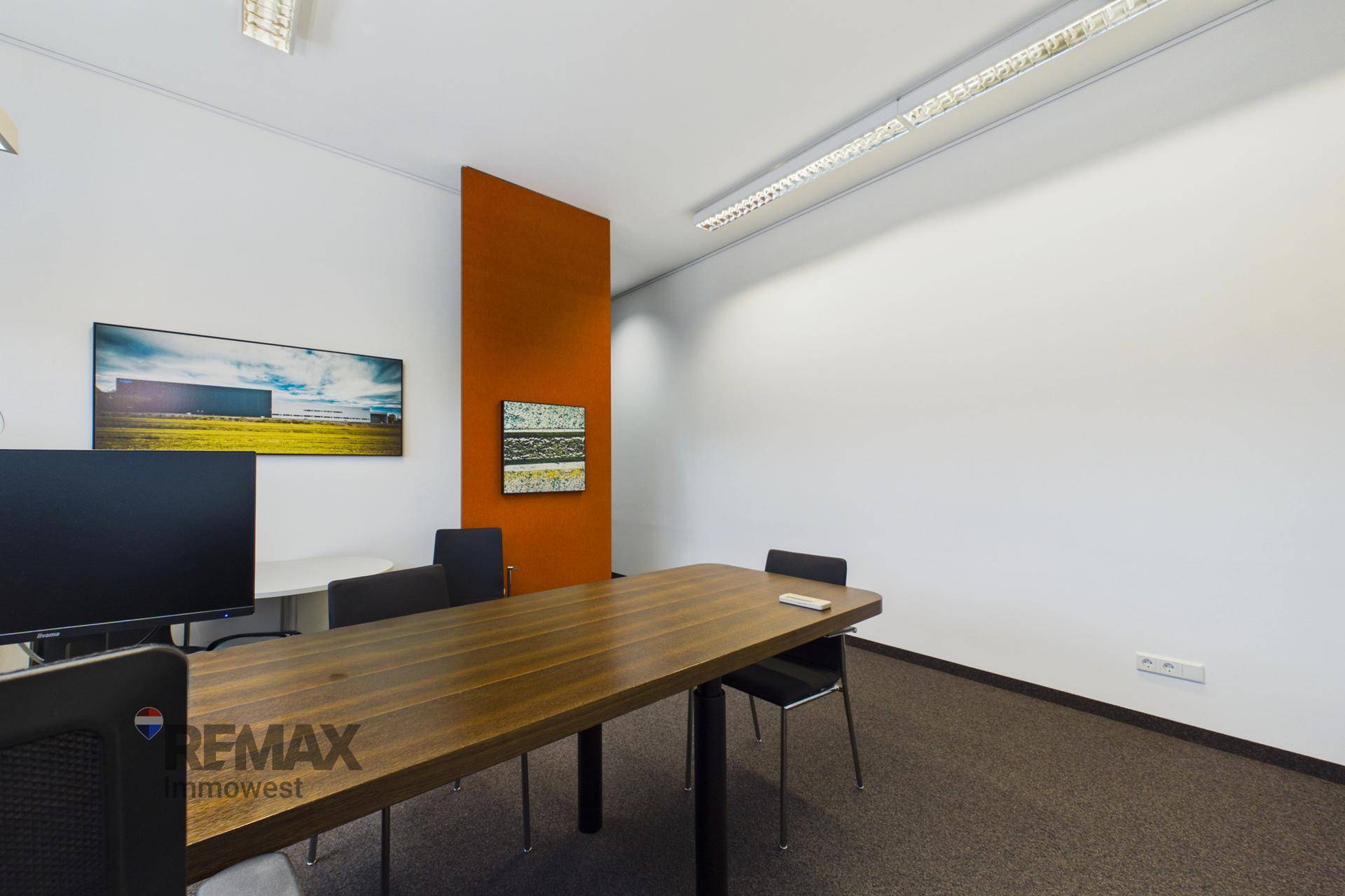 Modernes Büro mit einem langen Holztisch, schwarzen Stühlen und einem auffälligen orangefarbenen Wandelement.