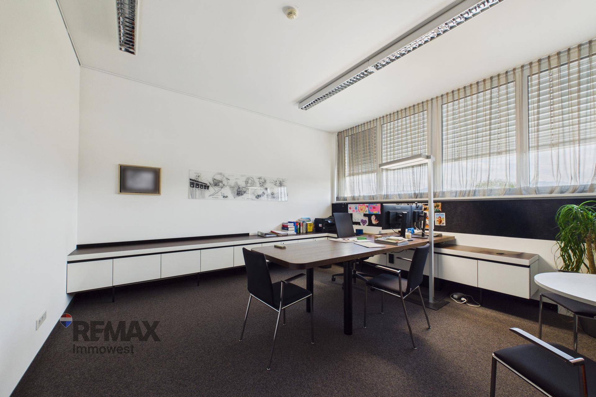 Helles Büro mit langem Schreibtisch, integrierten Schränken und großen Fenstern für viel Tageslicht.