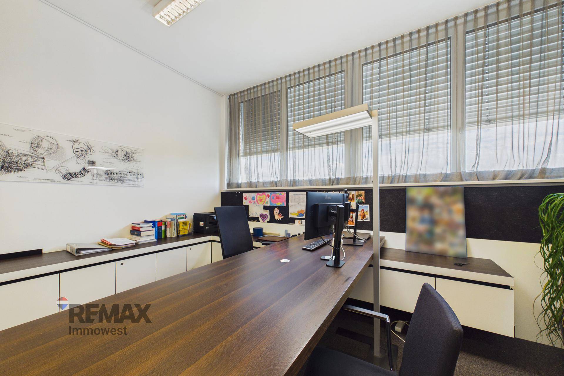 Detailansicht eines Arbeitsplatzes mit Computern, Dokumenten und Blick durch die großen Fenster.