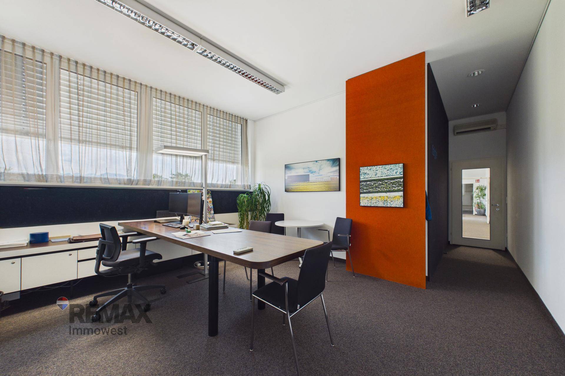 Geräumiges Einzelbüro mit großem Schreibtisch, modernen Möbeln und einem farbigen Akzent an der Wand.