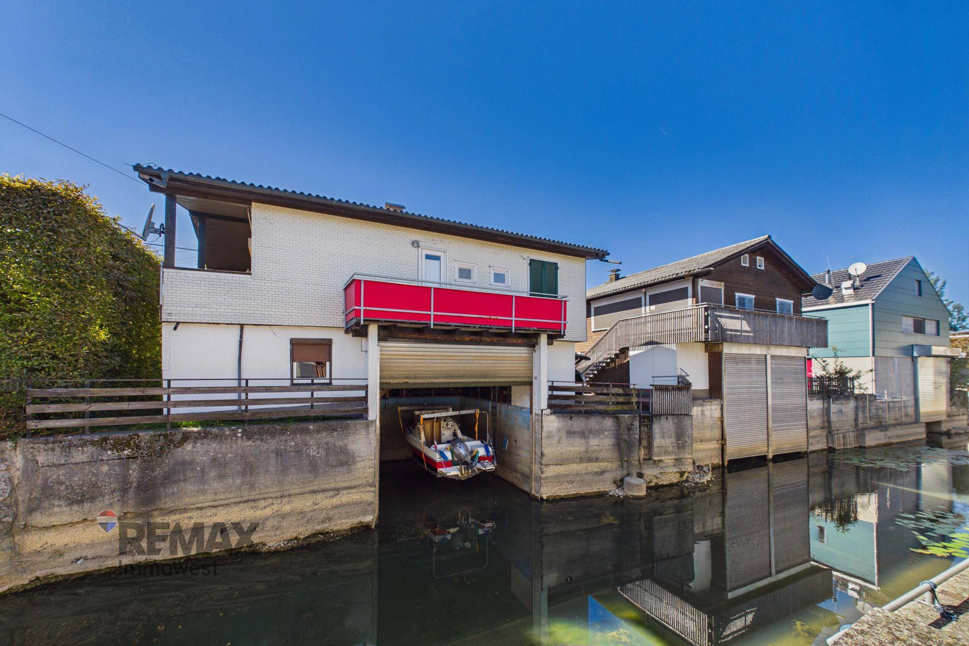 Ansicht des Hauses mit Bootsgarage direkt am Kanal und einem kleinen roten Balkon.
