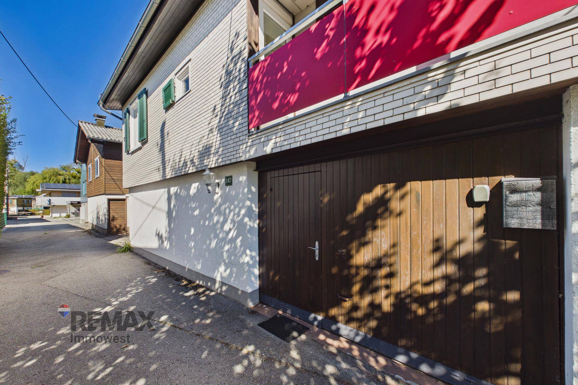 Seitenansicht des Hauses mit einer großen Holzgarage und einem roten Balkon im Obergeschoss.