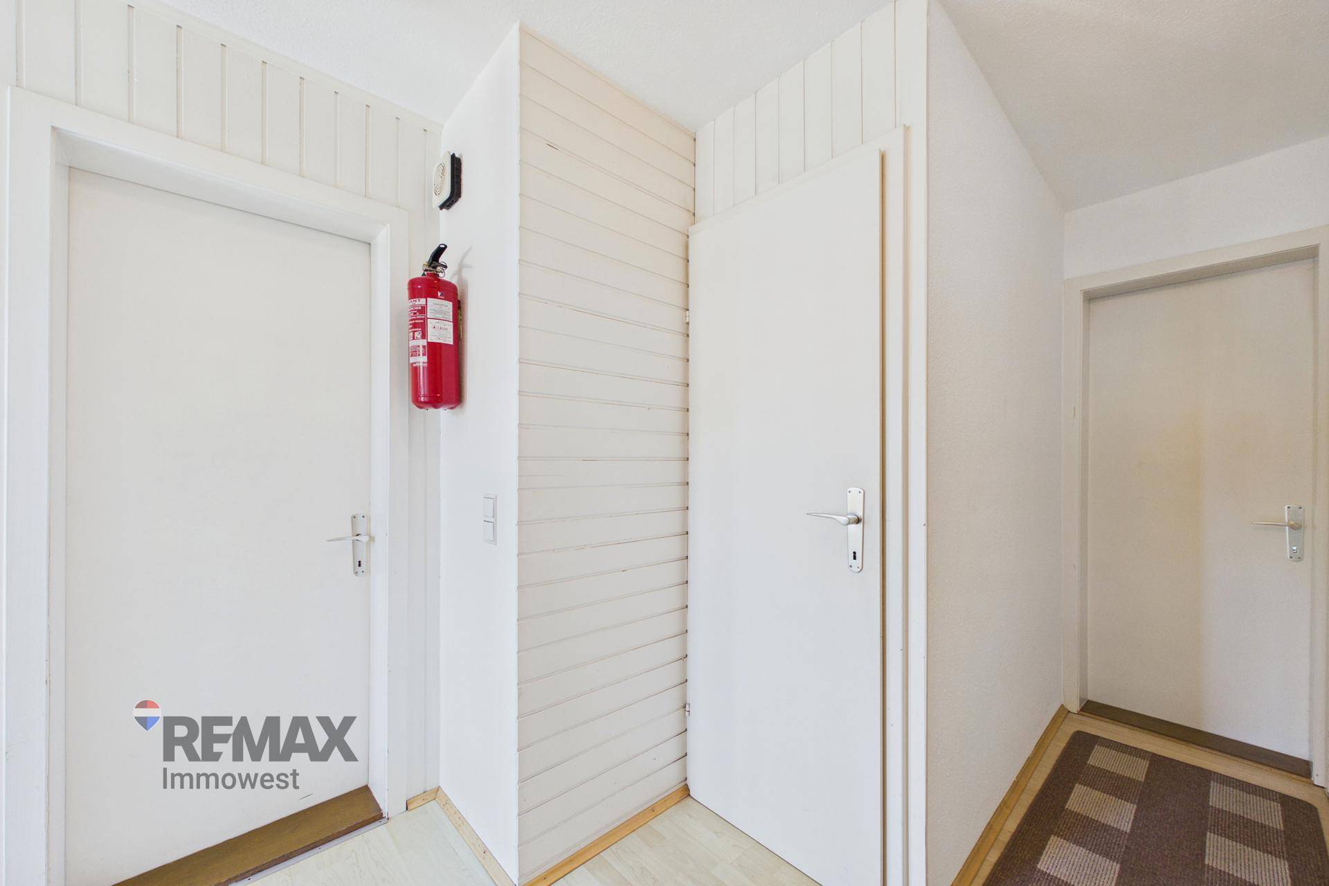 Schlichter Flur mit weißen Türen und einem Feuerlöscher an der Wand.