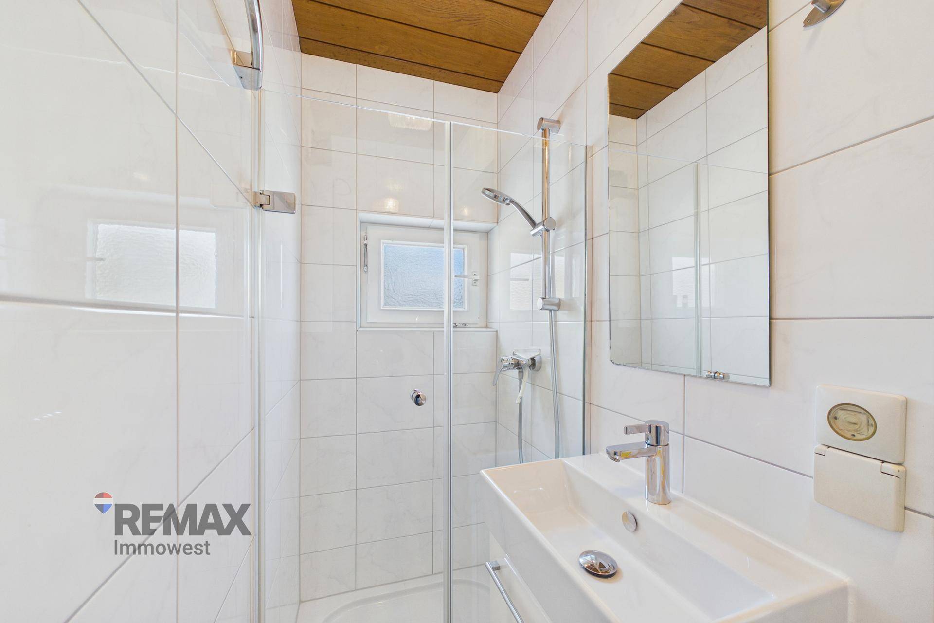 Modernes Badezimmer mit weiß gefliesten Wänden, Dusche und Waschbecken.