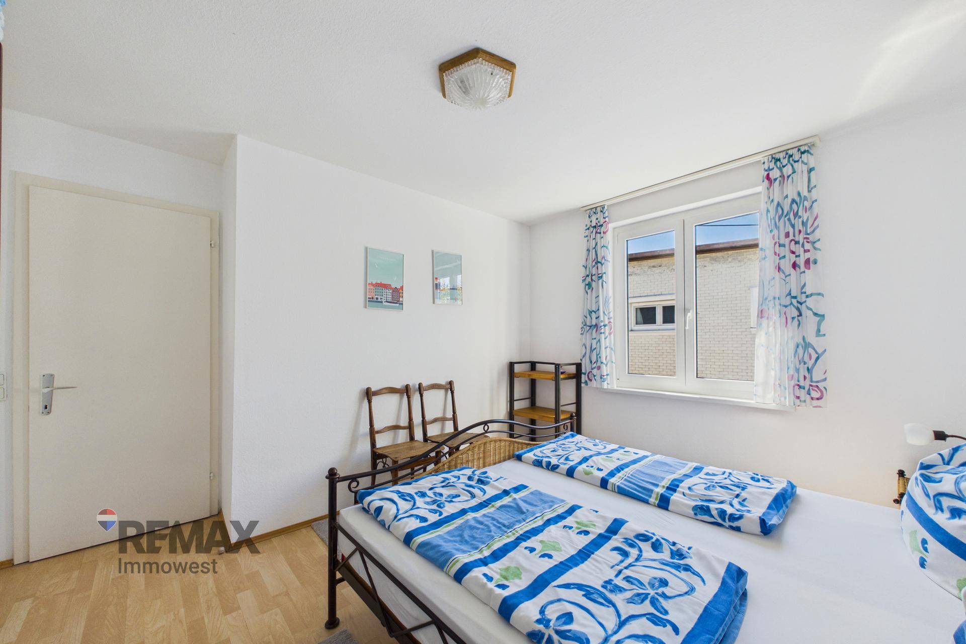 Helles Schlafzimmer mit Doppelbett, weißer Tür und Fenster mit Vorhängen.