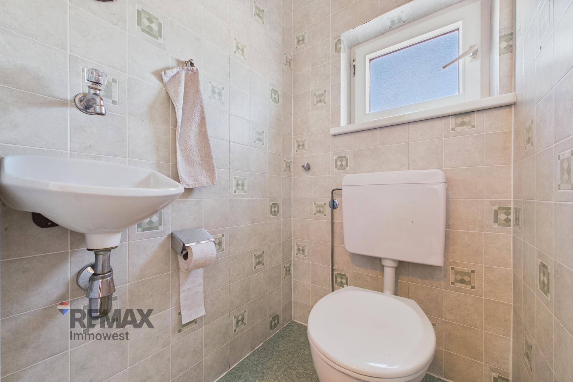 Kleines WC mit Toilette, Waschbecken und gemusterten Fliesen an den Wänden.