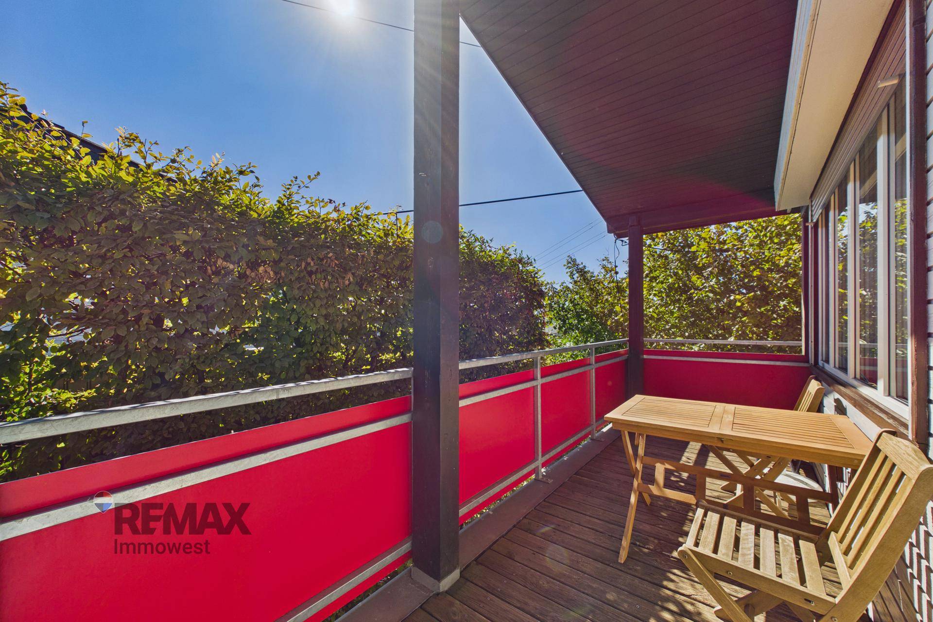 Sonniger Balkon mit Holztisch und Stühlen, umgeben von grünen Hecken.