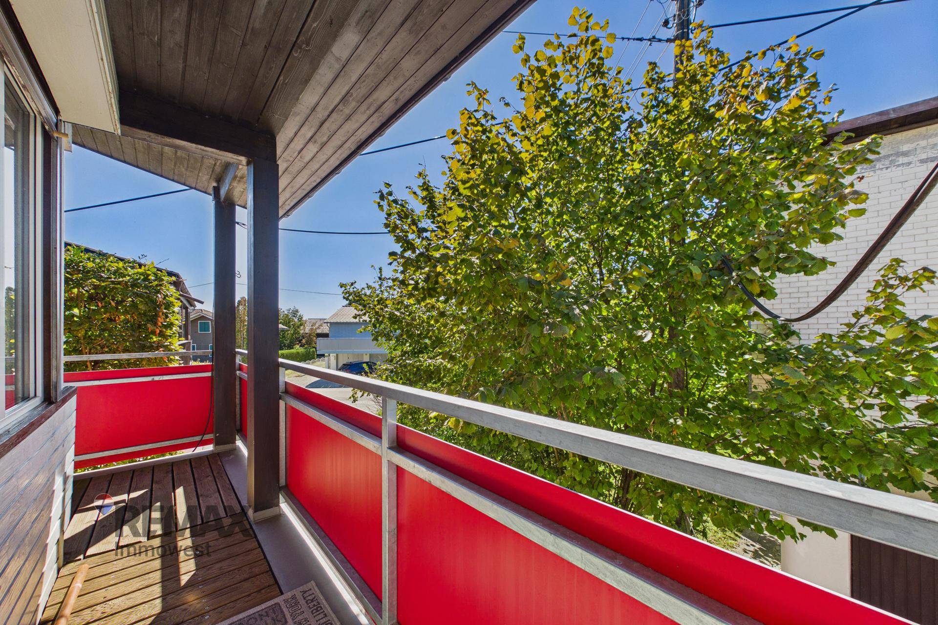 Überdachter Balkon mit Holzboden und Blick auf Bäume und die Umgebung.