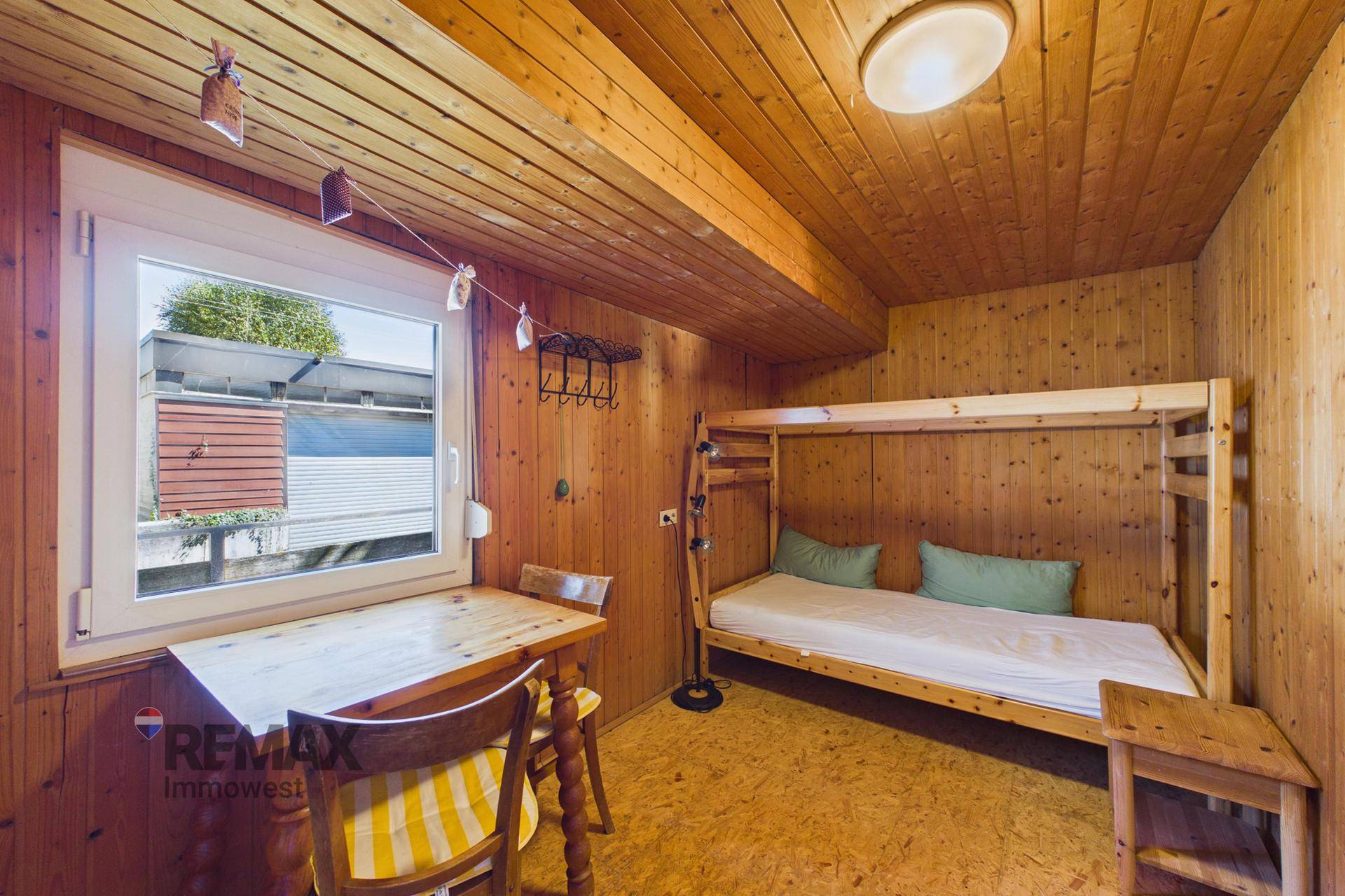 Kleines Zimmer mit Etagenbett, Holztisch und Fenster, komplett mit Holz verkleidet.