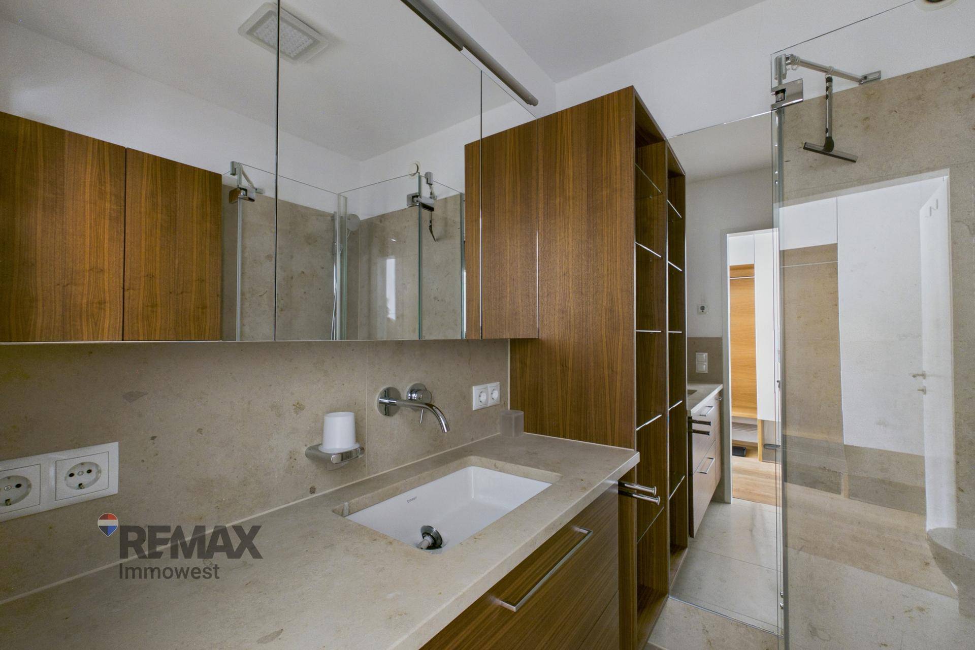 Modernes Badezimmer mit Steinwaschtisch, Holzschränken und einer begehbaren Dusche mit Glasabtrennung.