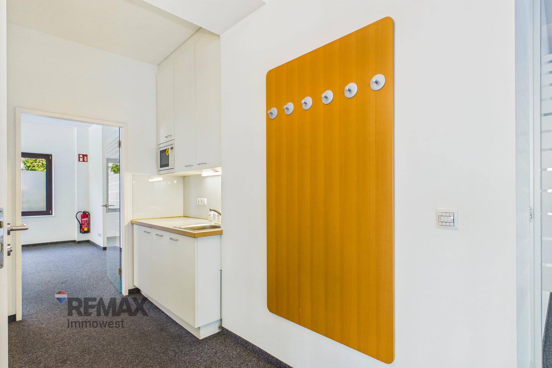Kompakte Küchenzeile mit Spüle und Mikrowelle, ergänzt durch eine Garderobe an der Wand.