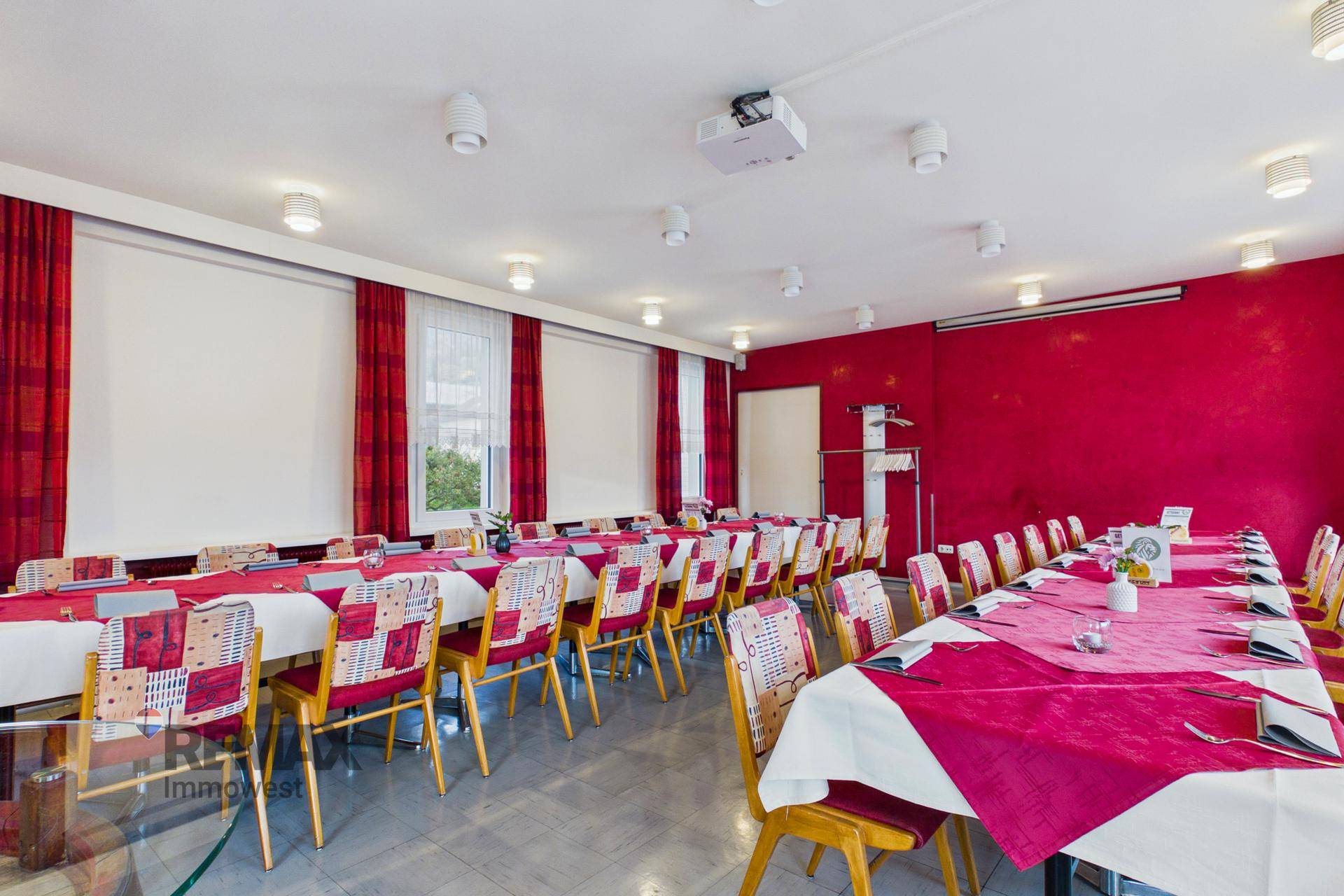 Geräumiger Speisesaal mit langen Tischen, roten Tischdecken und einem Projektor an der Decke.