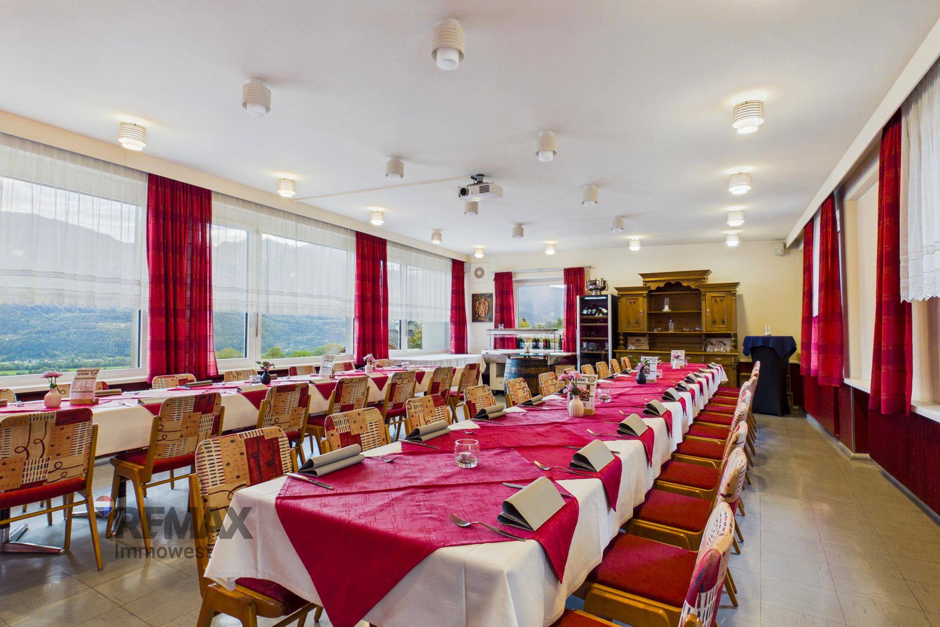 Heller Speisesaal mit Panoramablick auf die Berge, festlich gedeckten Tischen und roten Vorhängen.