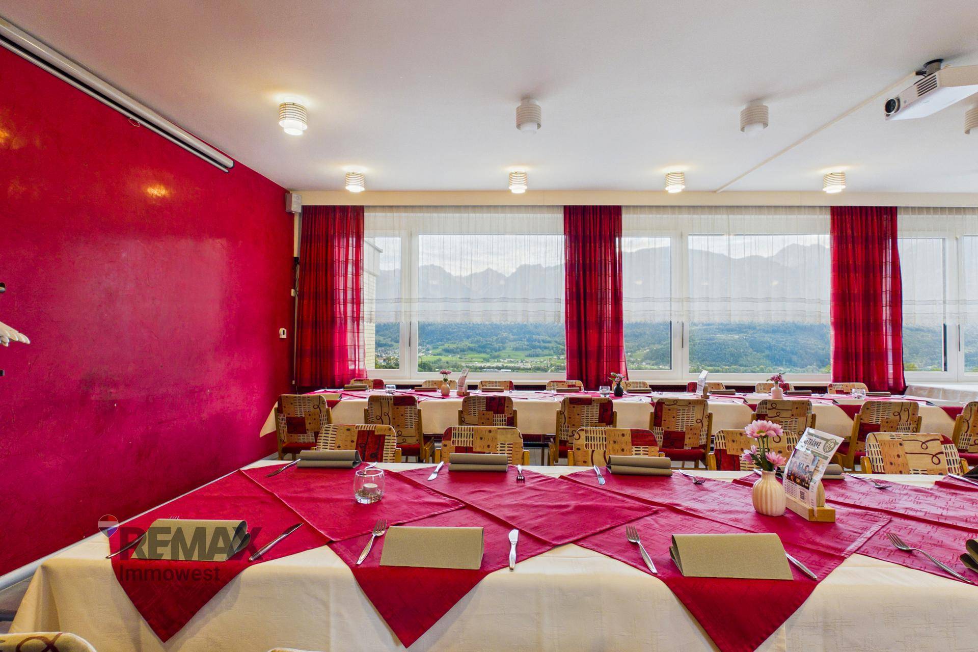 Großer Speisesaal mit vielen Tischen, roten Vorhängen und weitem Blick auf die Landschaft.