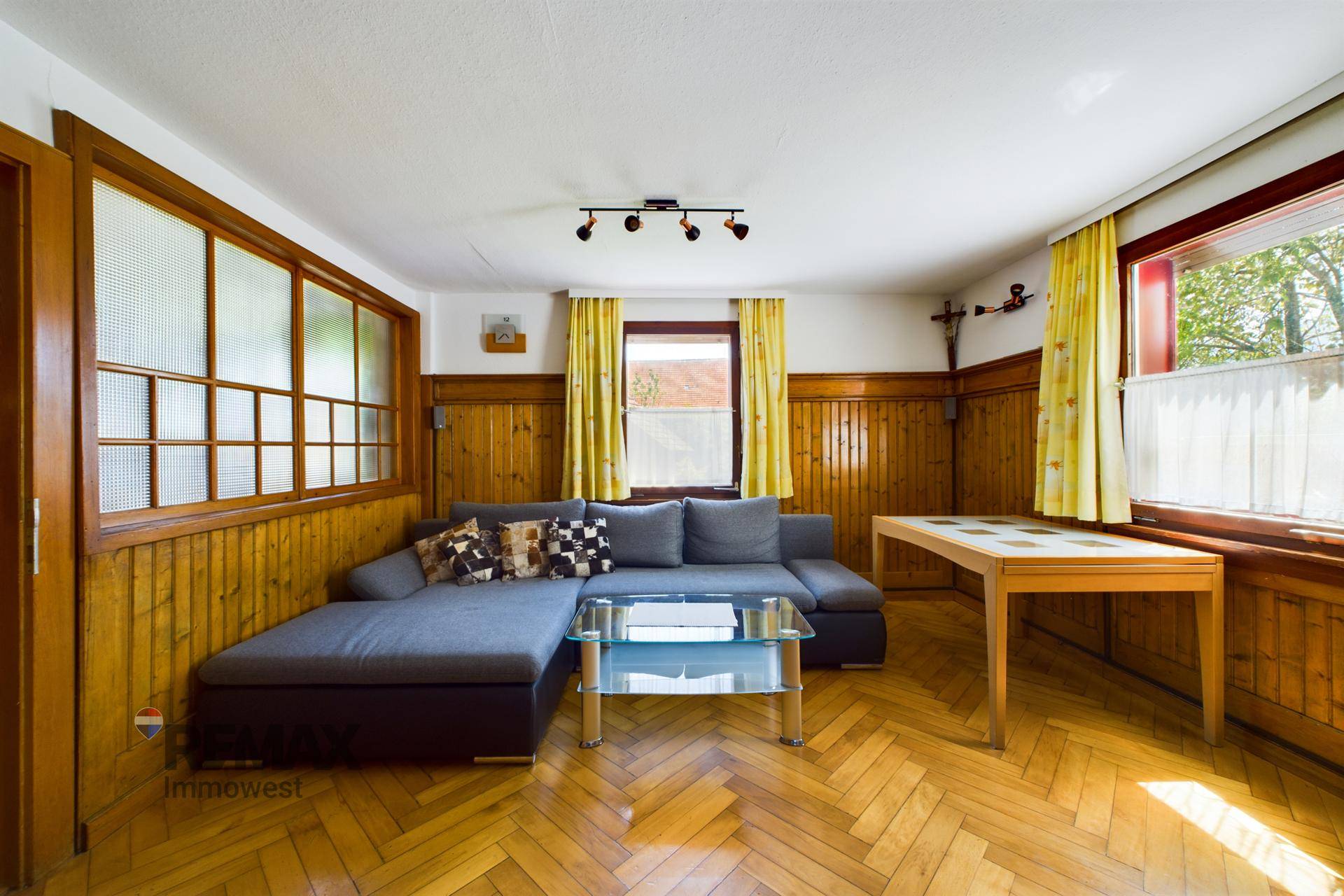 Gemütliches Wohnzimmer mit Holzboden, Holztäfelung und einem bequemen Ecksofa.