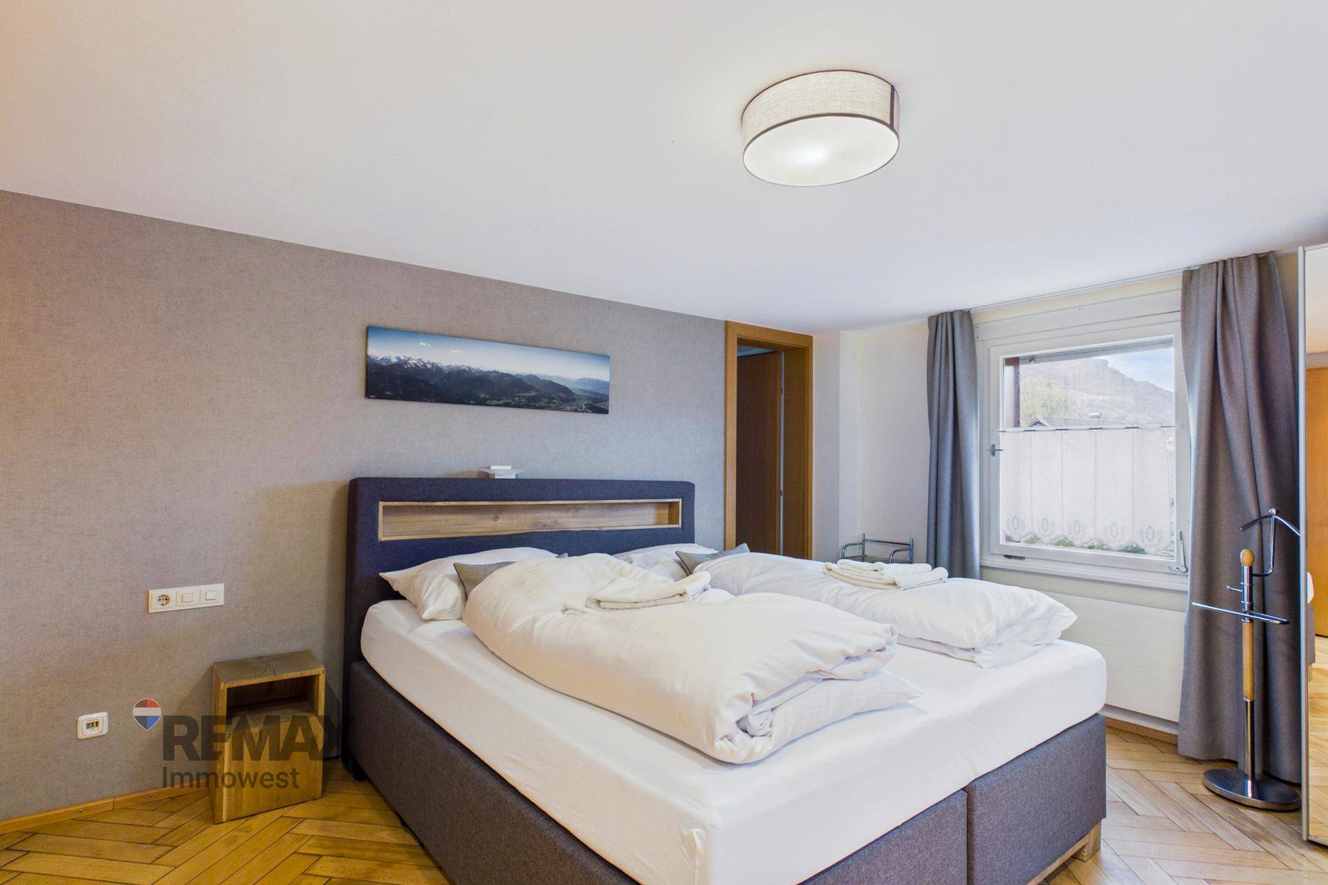 Schlafzimmer mit Doppelbett, Holzboden und einem Fenster mit Blick auf die Umgebung.