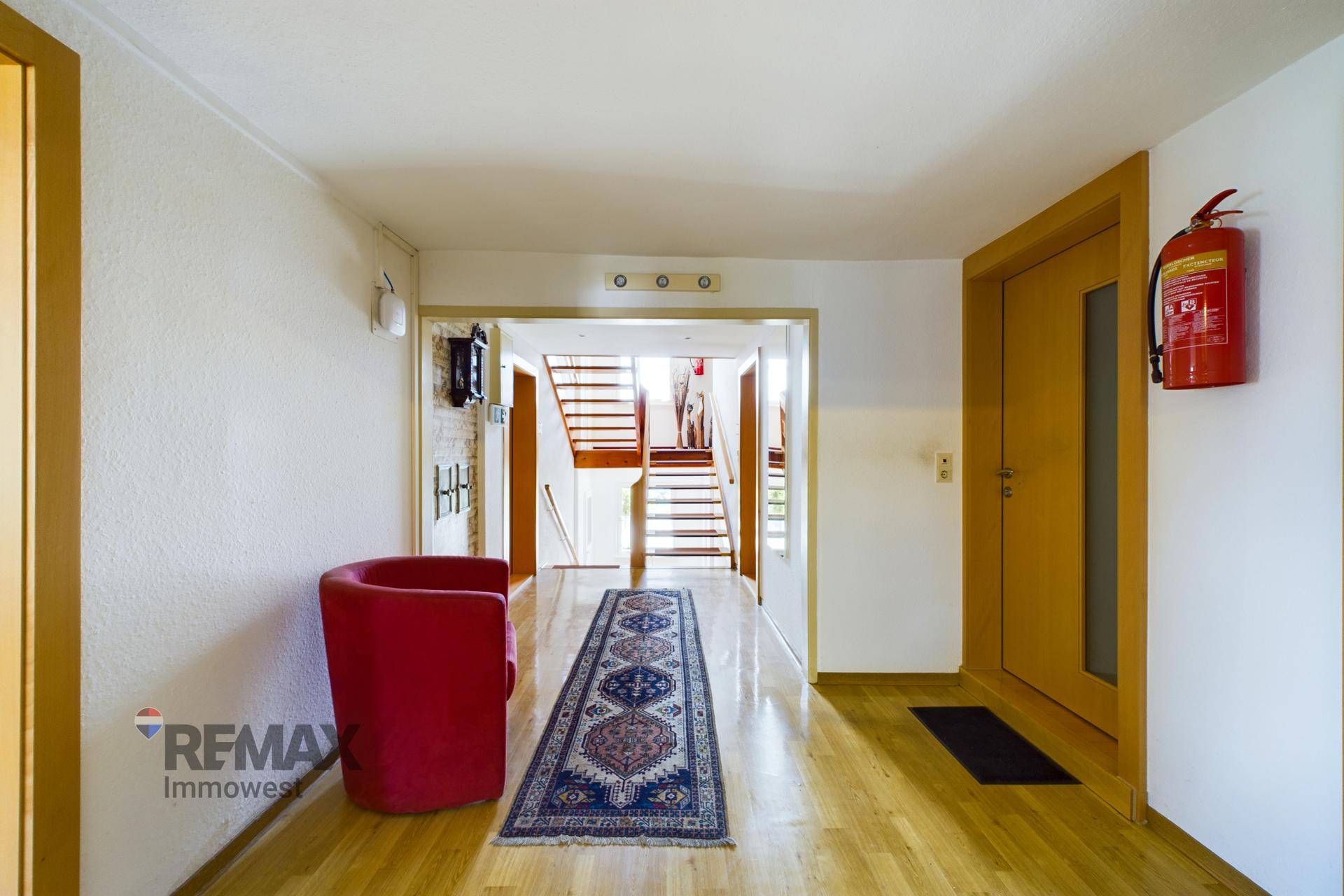 Geräumiger Flur mit Holzfußboden, einem roten Sessel und einer Treppe zum Obergeschoss.