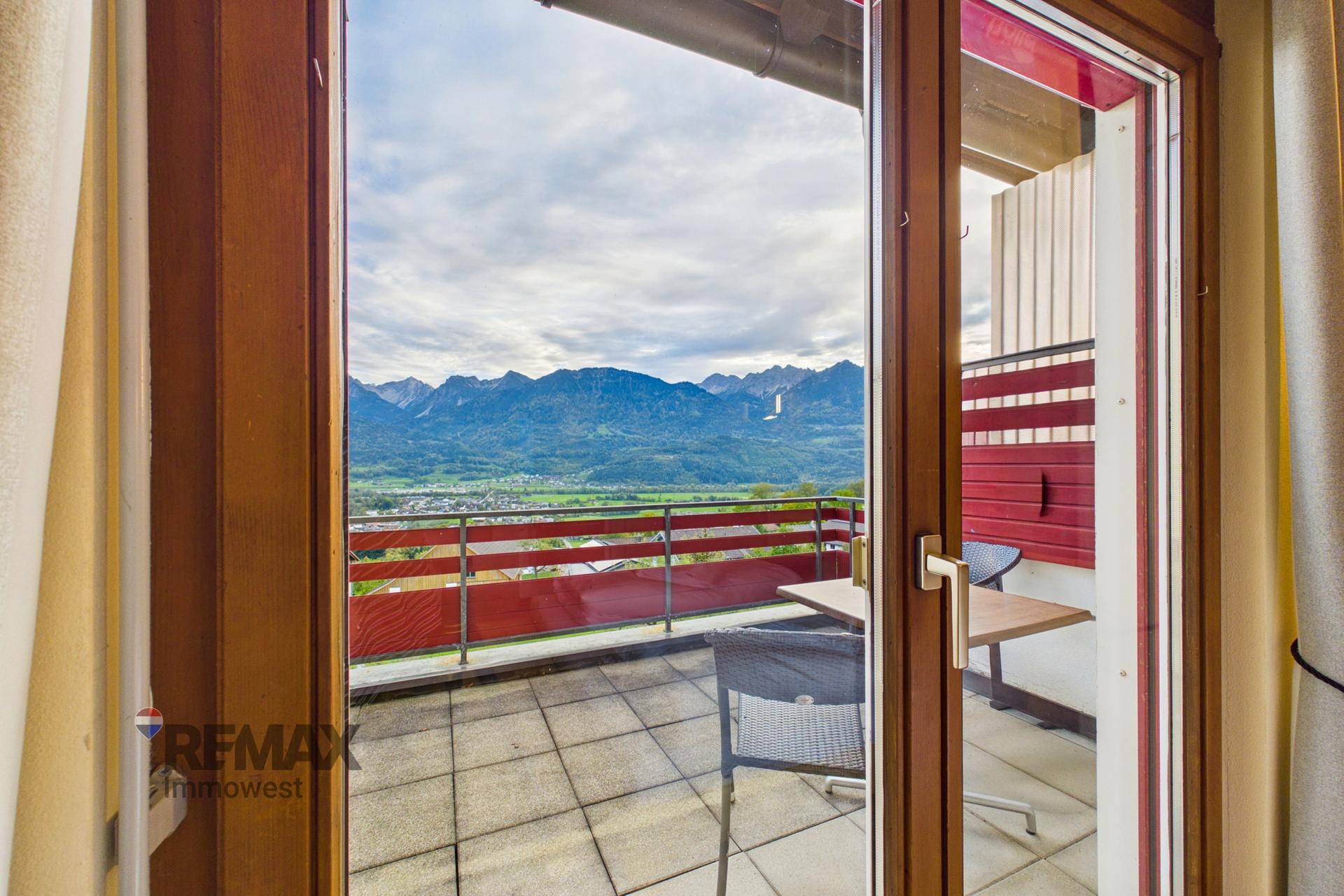 Blick vom Innenraum auf einen Balkon mit Bergblick und Sitzgelegenheiten.
