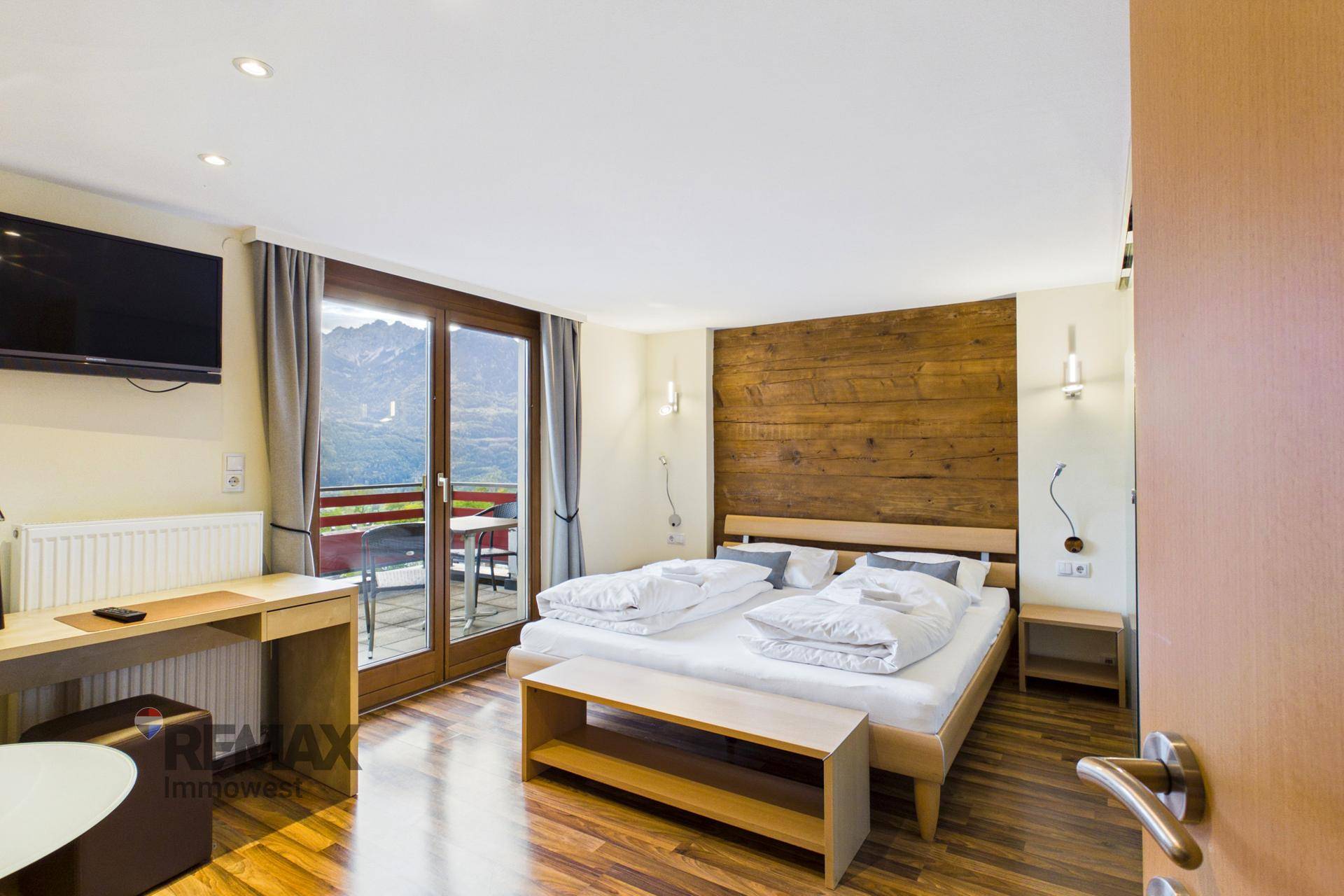 Schlafzimmer mit Holzwand, Doppelbett und Zugang zu einem Balkon mit Bergblick.