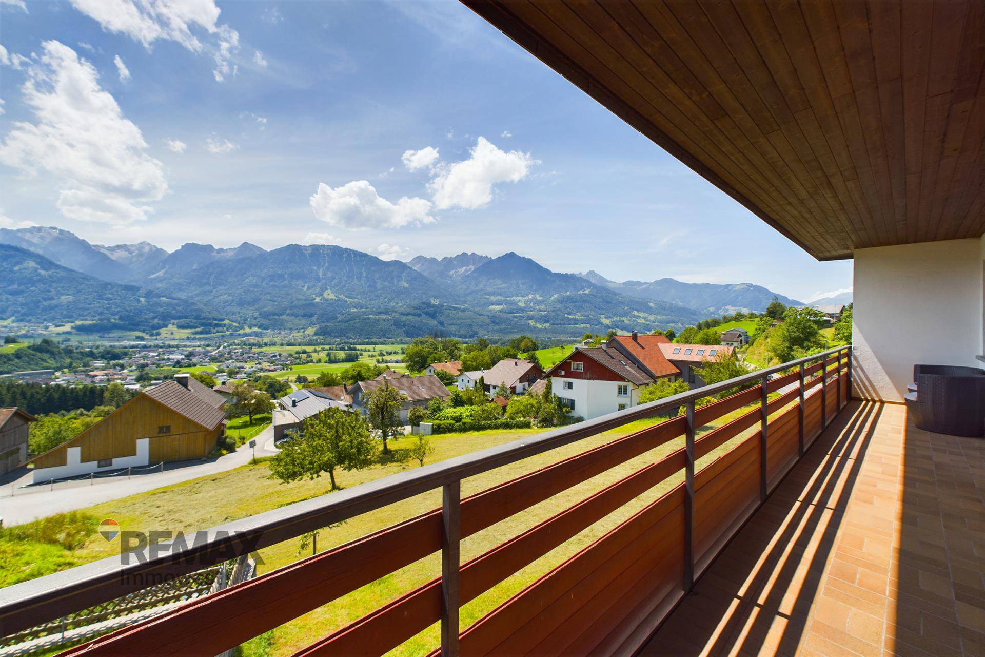 Langer Balkon mit Holzgeländer und atemberaubendem Blick auf die Berglandschaft und das Dorf.