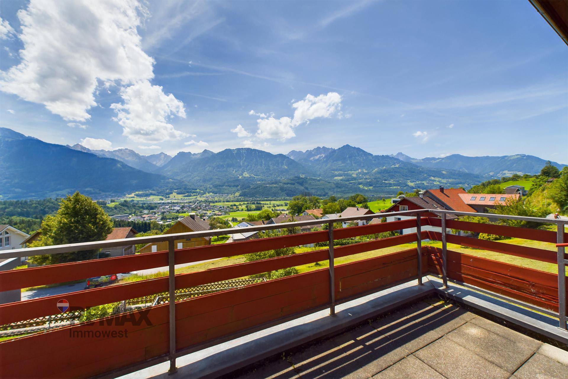 Großer Balkon mit weitem Blick auf die Berge und die umliegende Landschaft unter blauem Himmel.