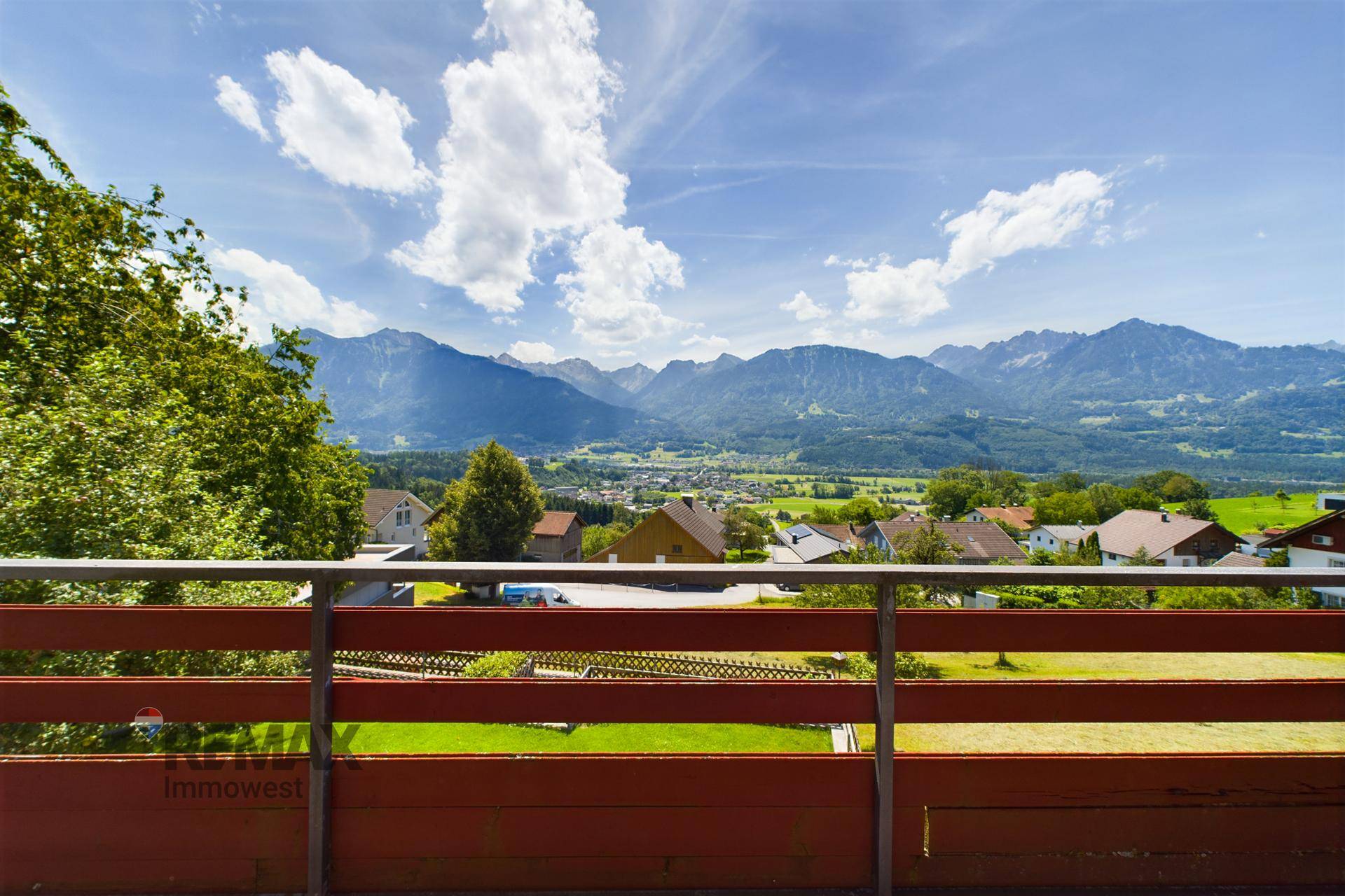Balkon mit Panoramablick auf die Alpen und das Tal, umgeben von grüner Natur.