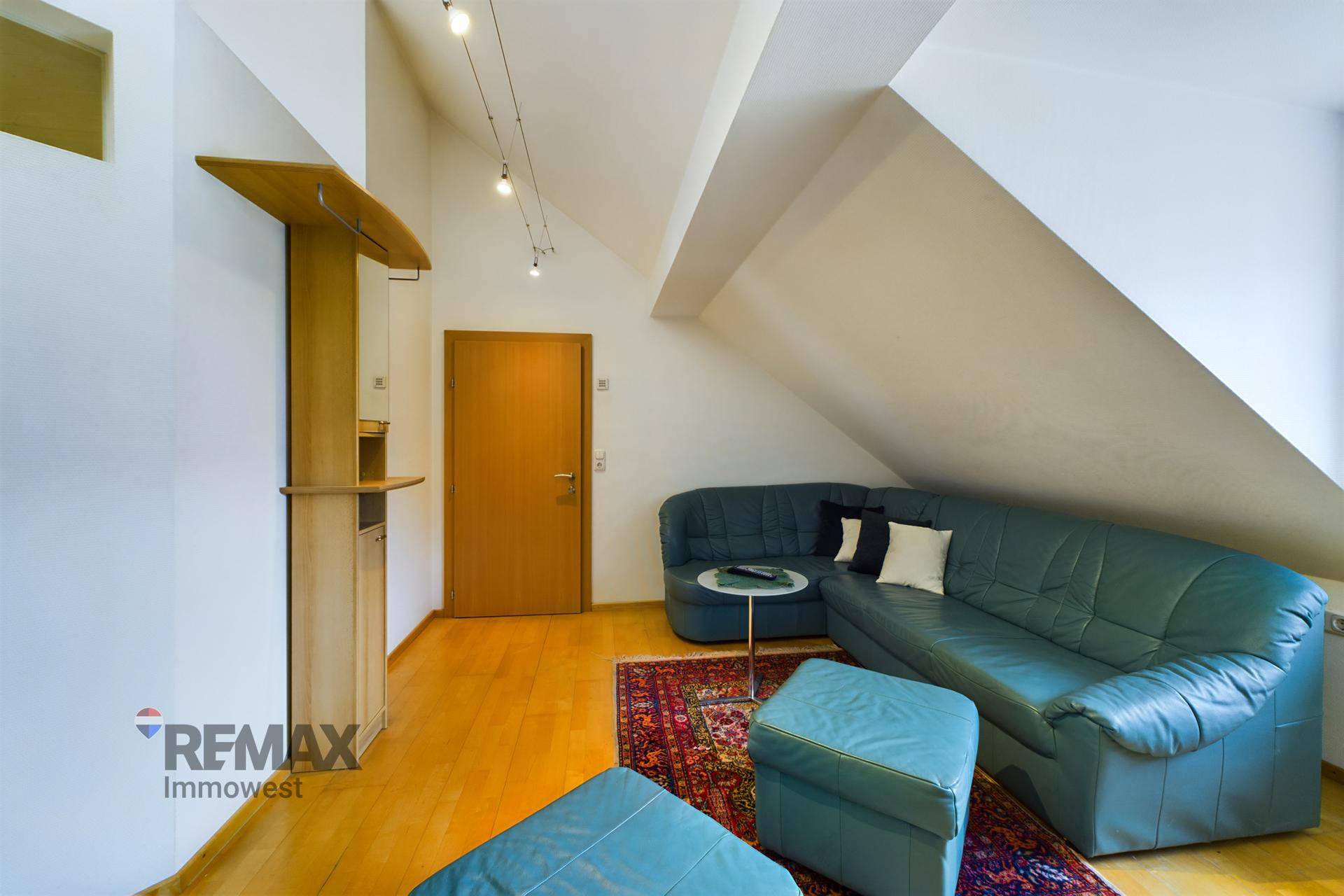 Gemütliches Wohnzimmer im Dachgeschoss mit blauer Ledercouch, Holzboden und schrägen Wänden.
