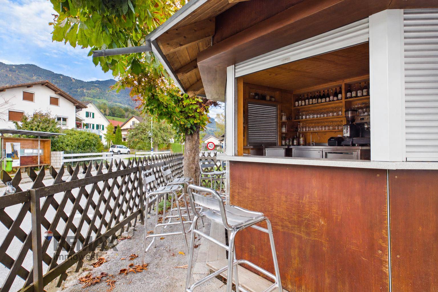 Außenbar mit Hockern und Blick auf die Straße sowie die umliegende Berglandschaft.