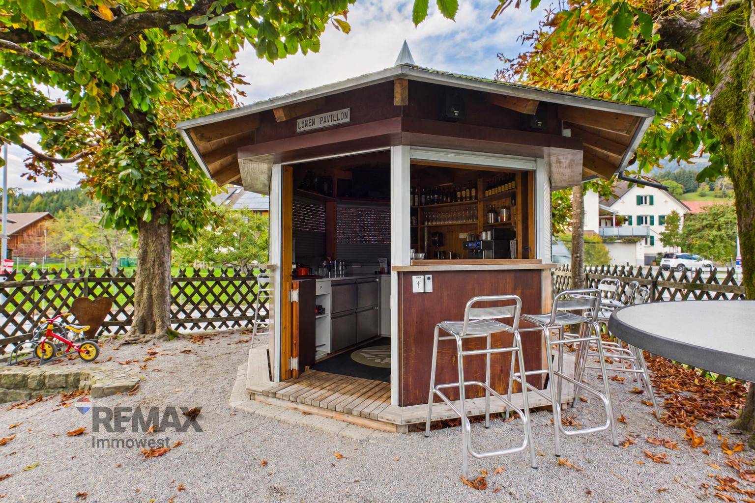 Freistehender Pavillon mit Bar und Sitzgelegenheiten im Außenbereich, umgeben von Bäumen.