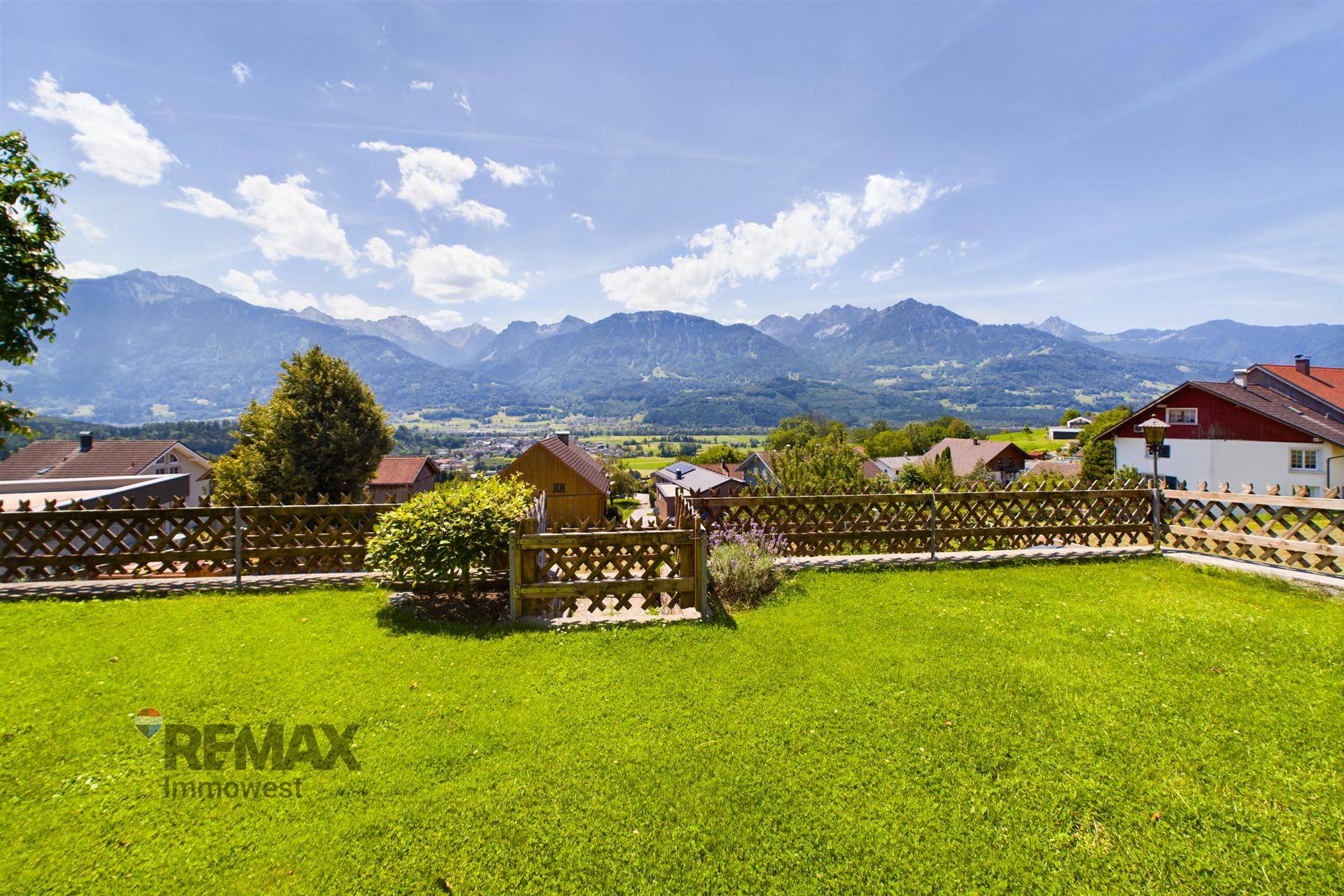 Weitläufige Rasenfläche mit Holzzaun und Panoramablick auf die umliegende Berglandschaft.