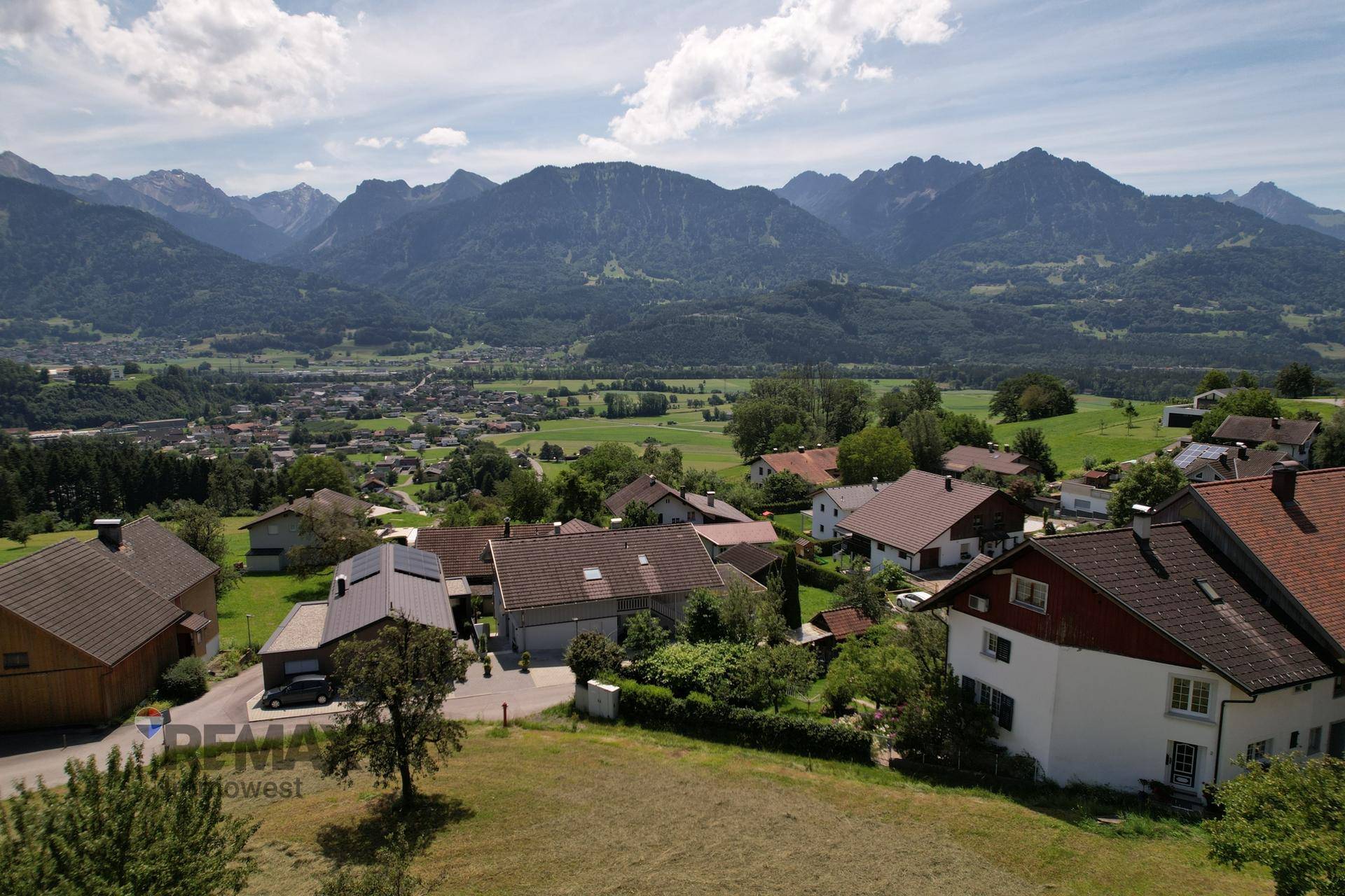 Weitläufige Luftaufnahme des Dorfes mit Häusern und der beeindruckenden Bergkulisse.