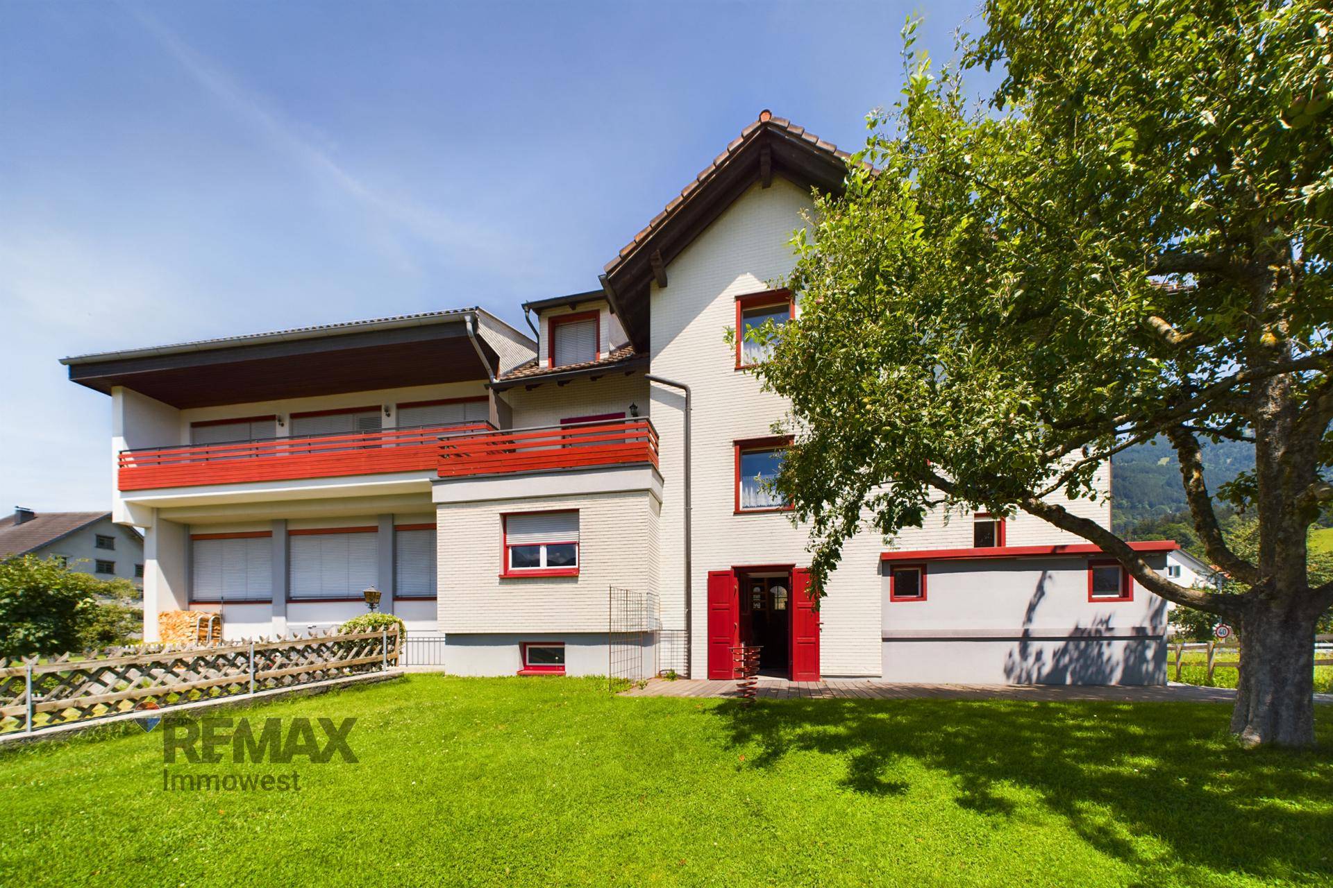 Gebäudeaußenansicht mit weißer Fassade, roten Akzenten und gepflegtem Rasenbereich.