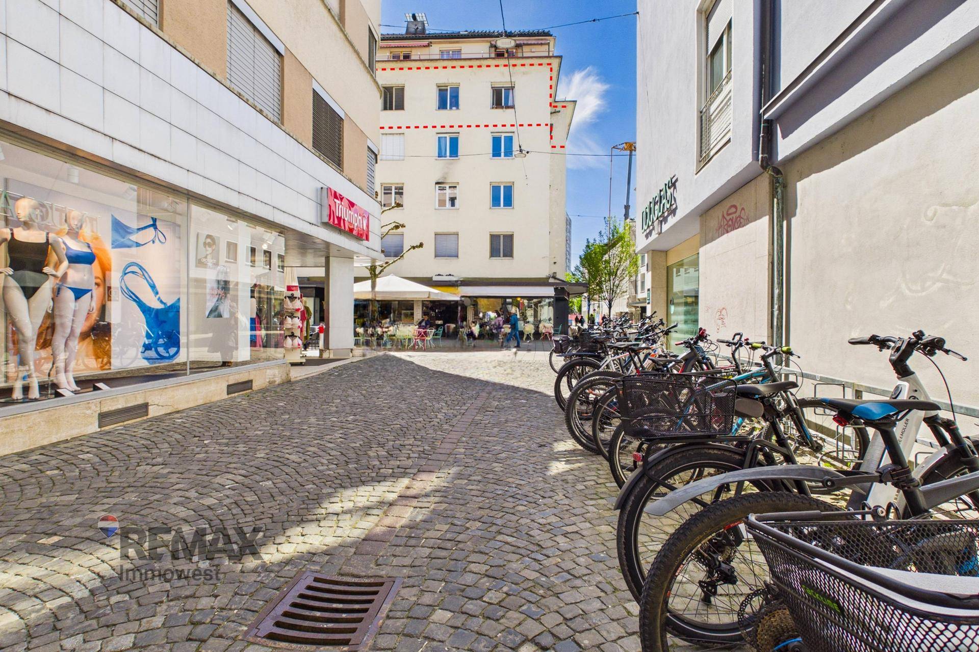 Gasse mit Fahrradständern und Blick auf die Rückseite eines Gebäudes mit Außengastronomie.