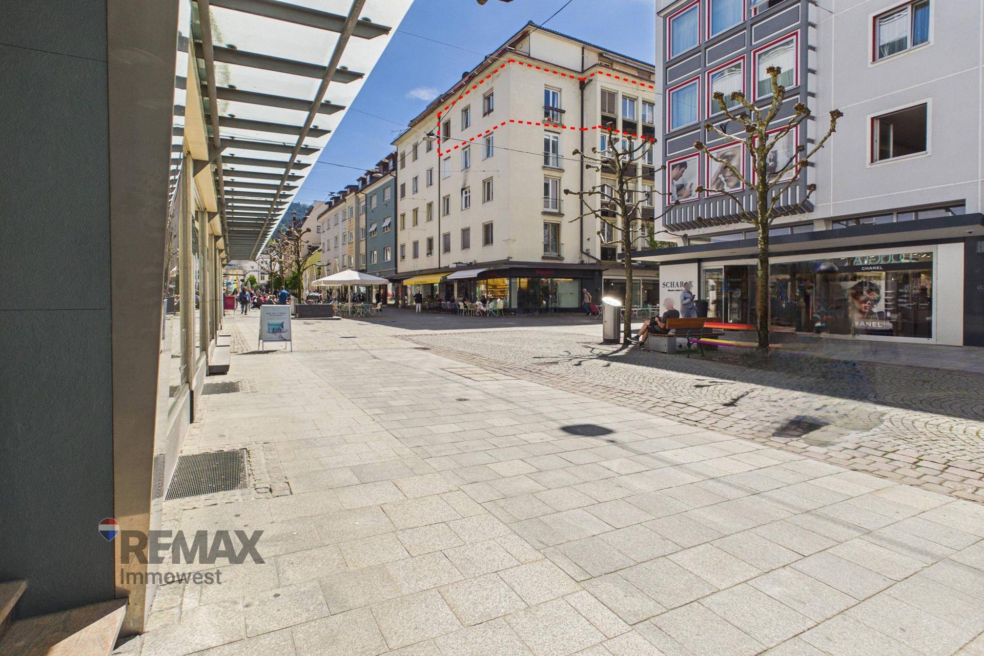 Blick auf eine belebte Einkaufsstraße mit Geschäften und dem Gebäude im Hintergrund.