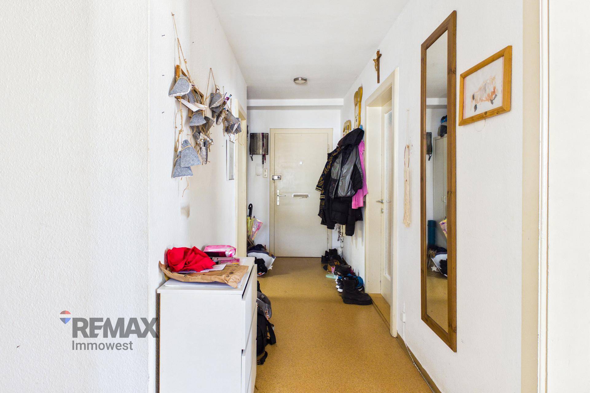 Langer Flur mit Garderobe, Spiegel und Linoleumboden.