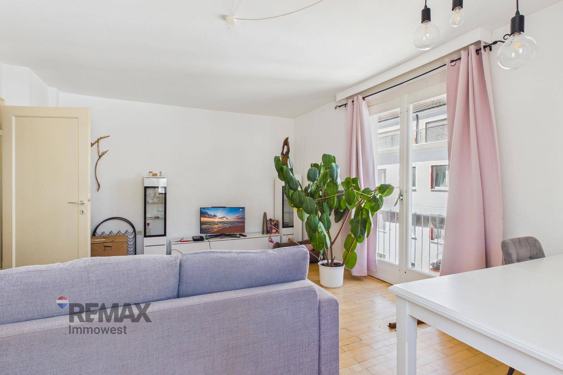 Heller Wohnbereich mit Sofa, Fernseher und Esstisch, Zugang zu einem französischen Balkon.