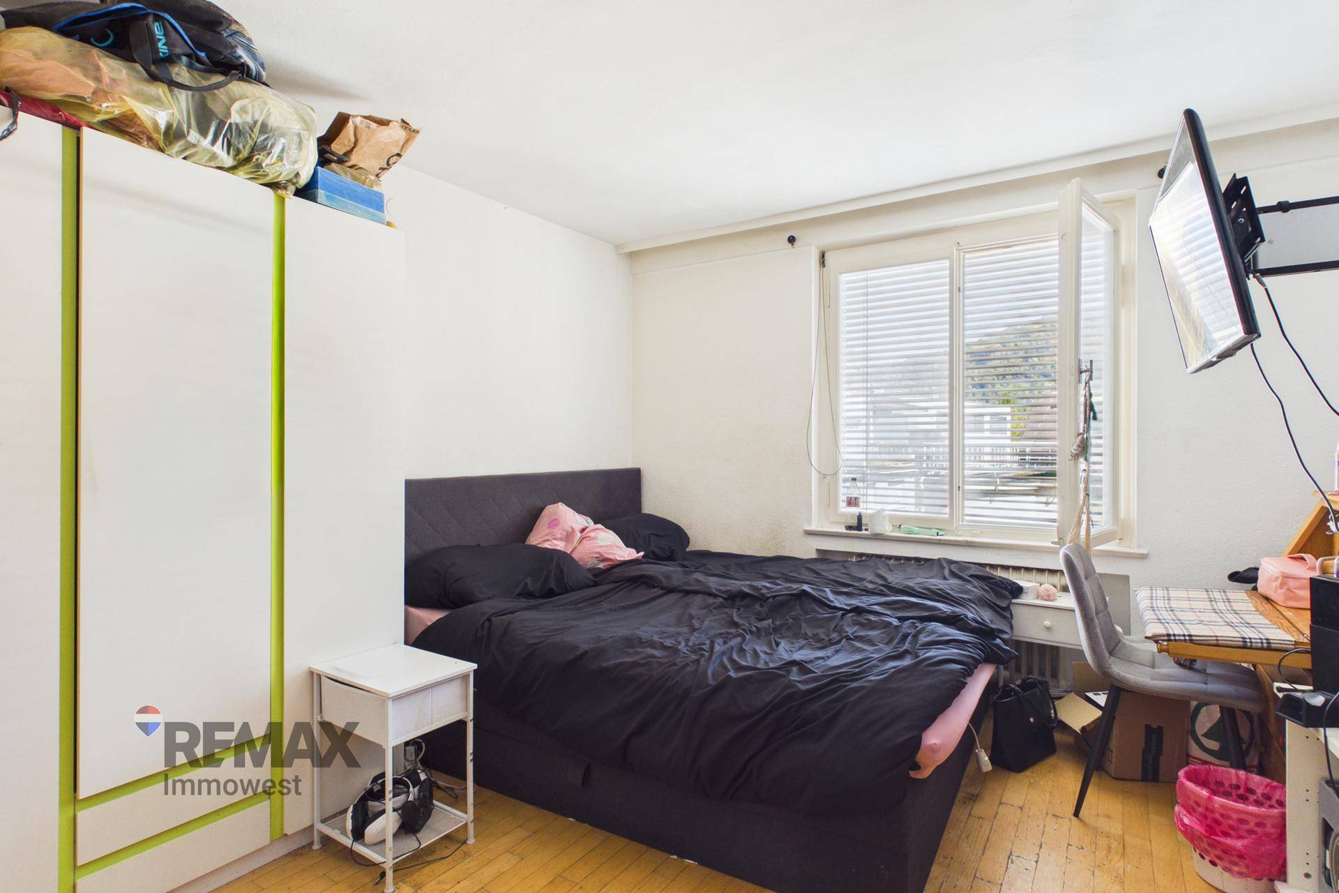 Schlafzimmer mit Doppelbett, Schrank und Schreibtisch, hell durch großes Fenster.