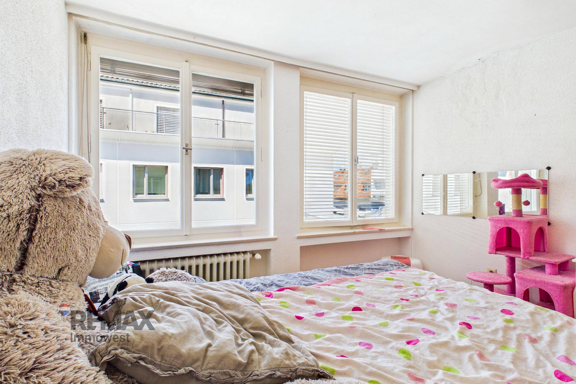 Helles Schlafzimmer mit großem Fenster und Blick auf die gegenüberliegenden Gebäude.