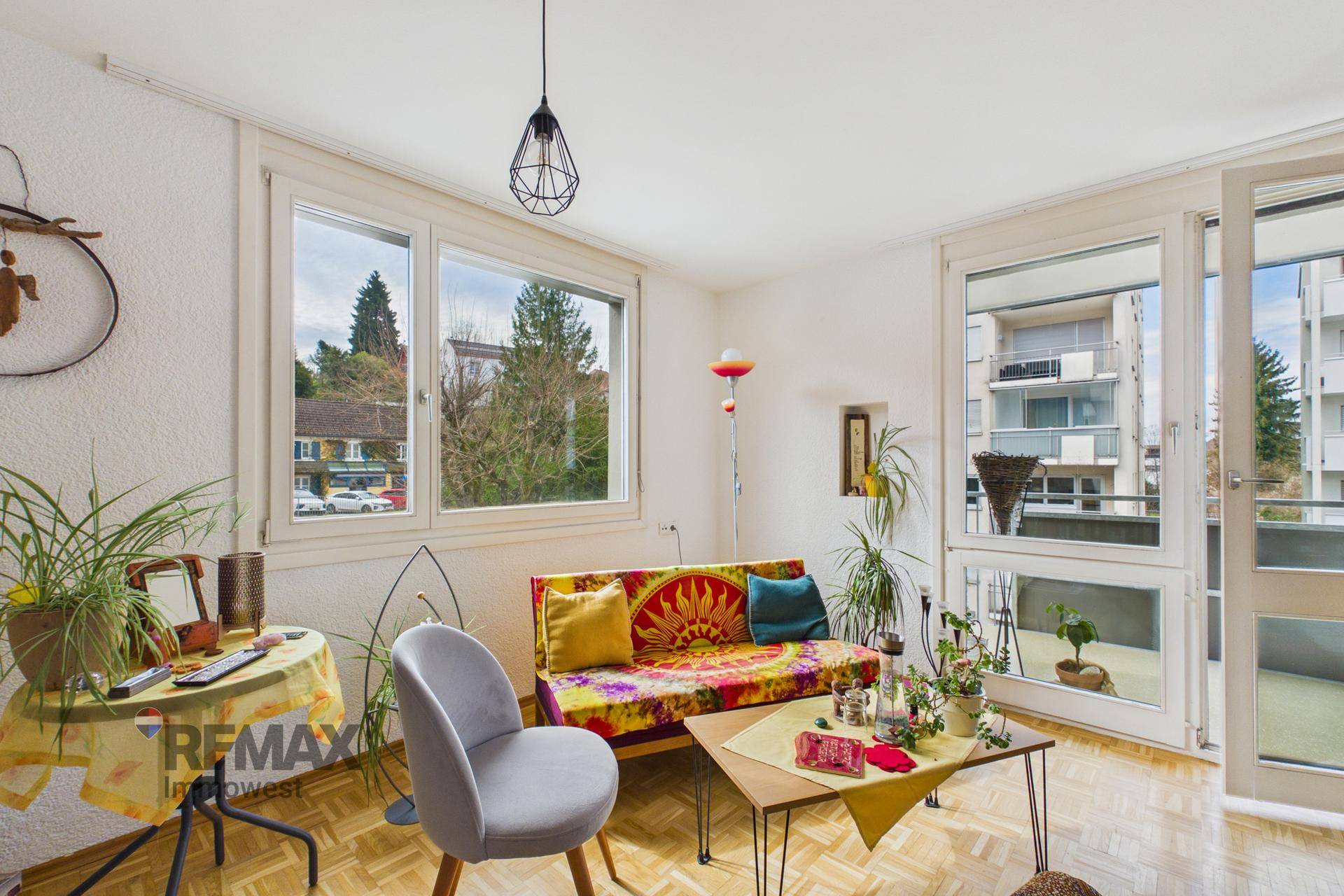 Wohnzimmer mit farbenfrohem Sofa, Parkettboden und Zugang zum Balkon.