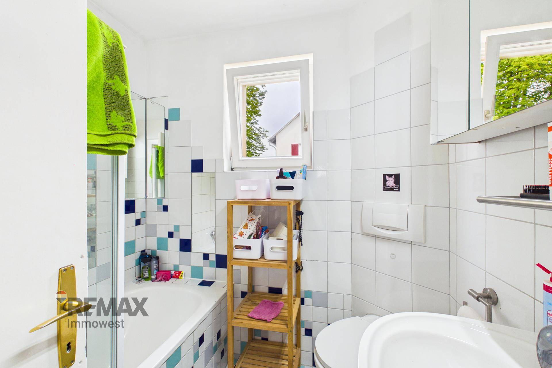 Badezimmer mit Badewanne, Fenster und farbigen Fliesen in Blau- und Türkistönen.