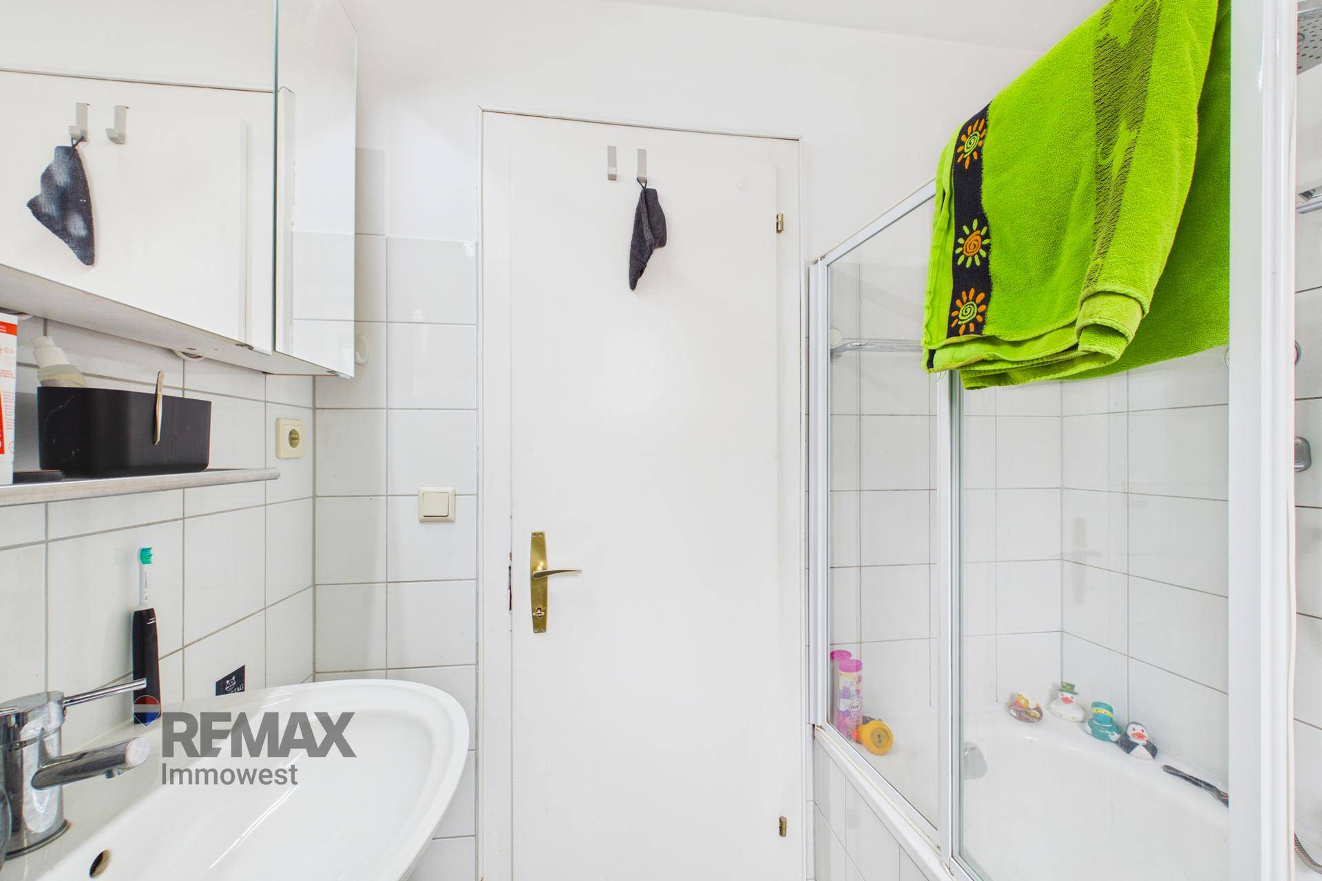 Badezimmer mit Duschbereich, Waschbecken und weißen Wandfliesen.