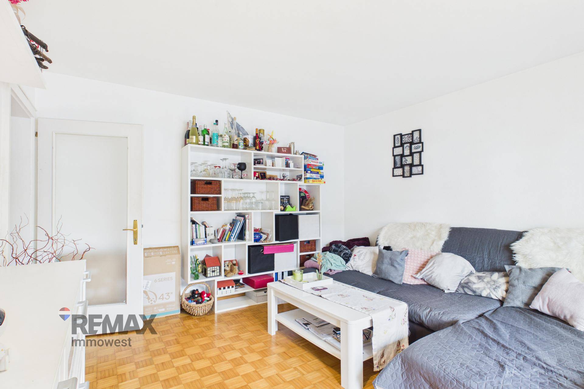 Wohnzimmer mit Sofa, Bücherregal und Parkettboden.