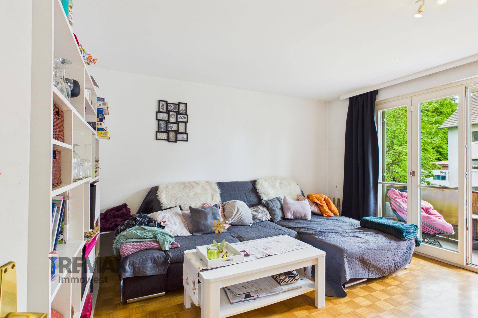 Gemütliches Wohnzimmer mit großem Sofa, Parkettboden und Zugang zum Balkon.