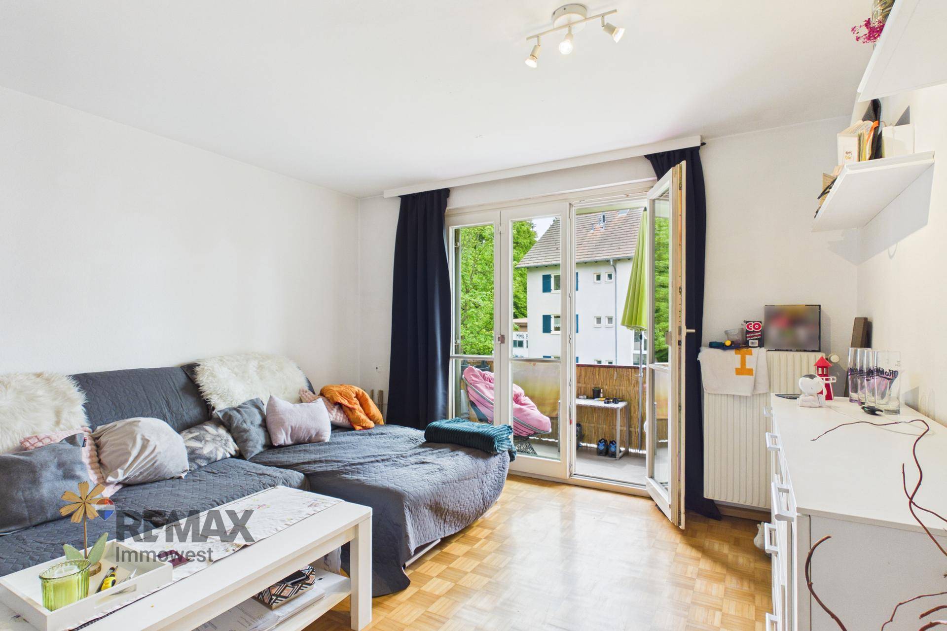 Helles Wohnzimmer mit Balkonzugang, Sofa und Parkettboden.